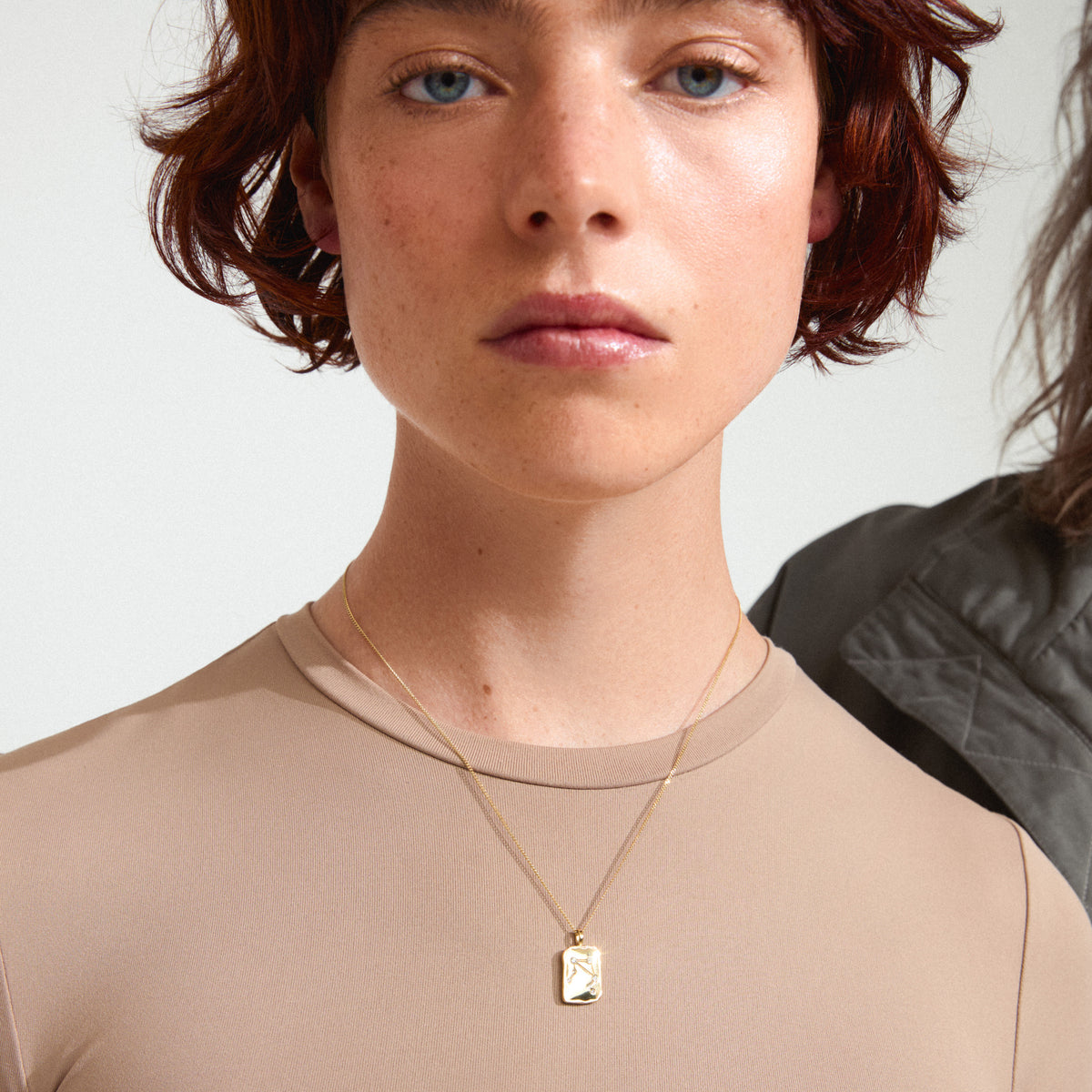 Woman with short red hair wearing the LIBRA Zodiac Sign necklace by Pilgrim, featuring a gold-plated coin pendant with Libra motif and sparkling constellation.
