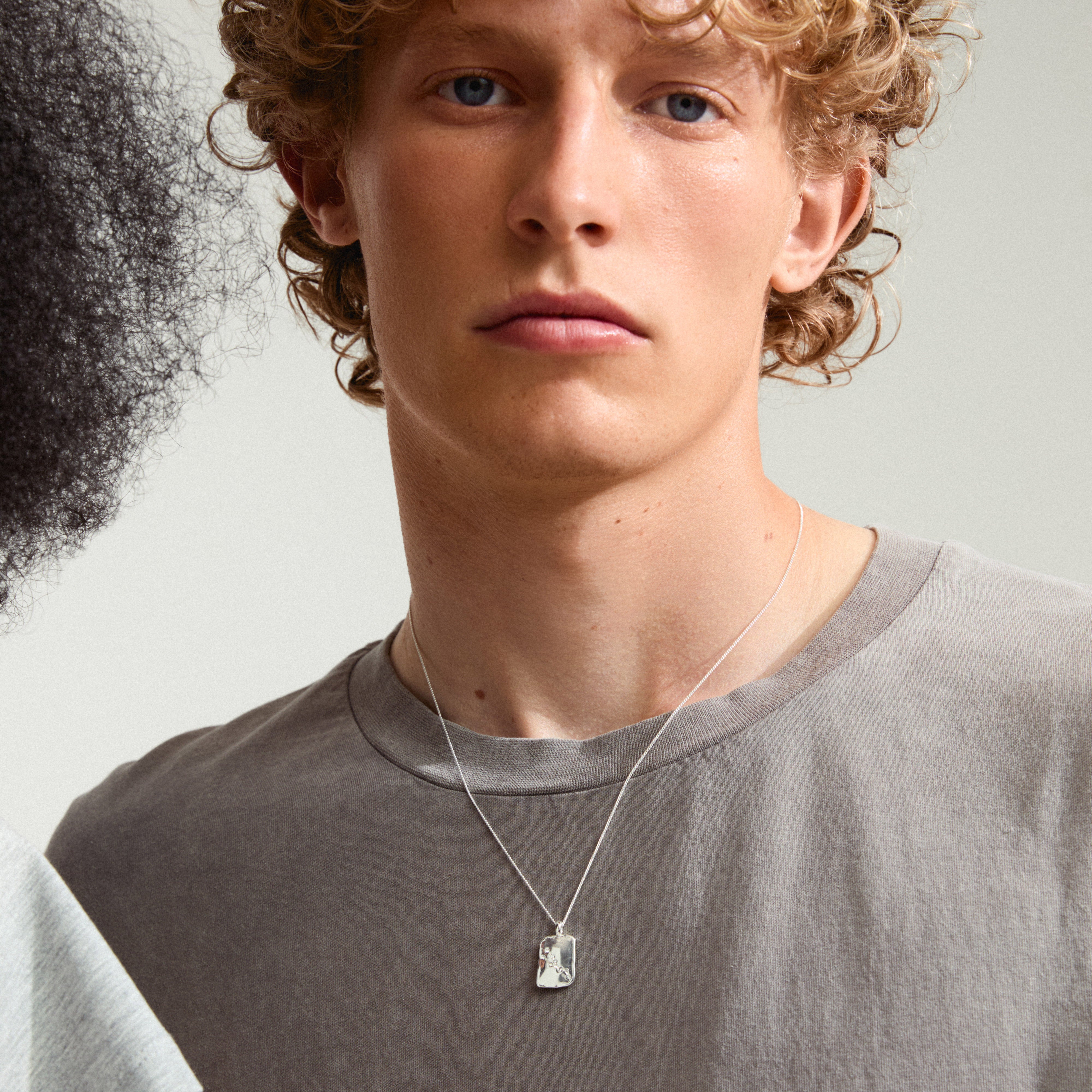 Curly-haired person wearing Pilgrim's TAURUS Zodiac Sign necklace, featuring a silver-plated chain with a square coin pendant showcasing a Taurus motif and crystal constellation.