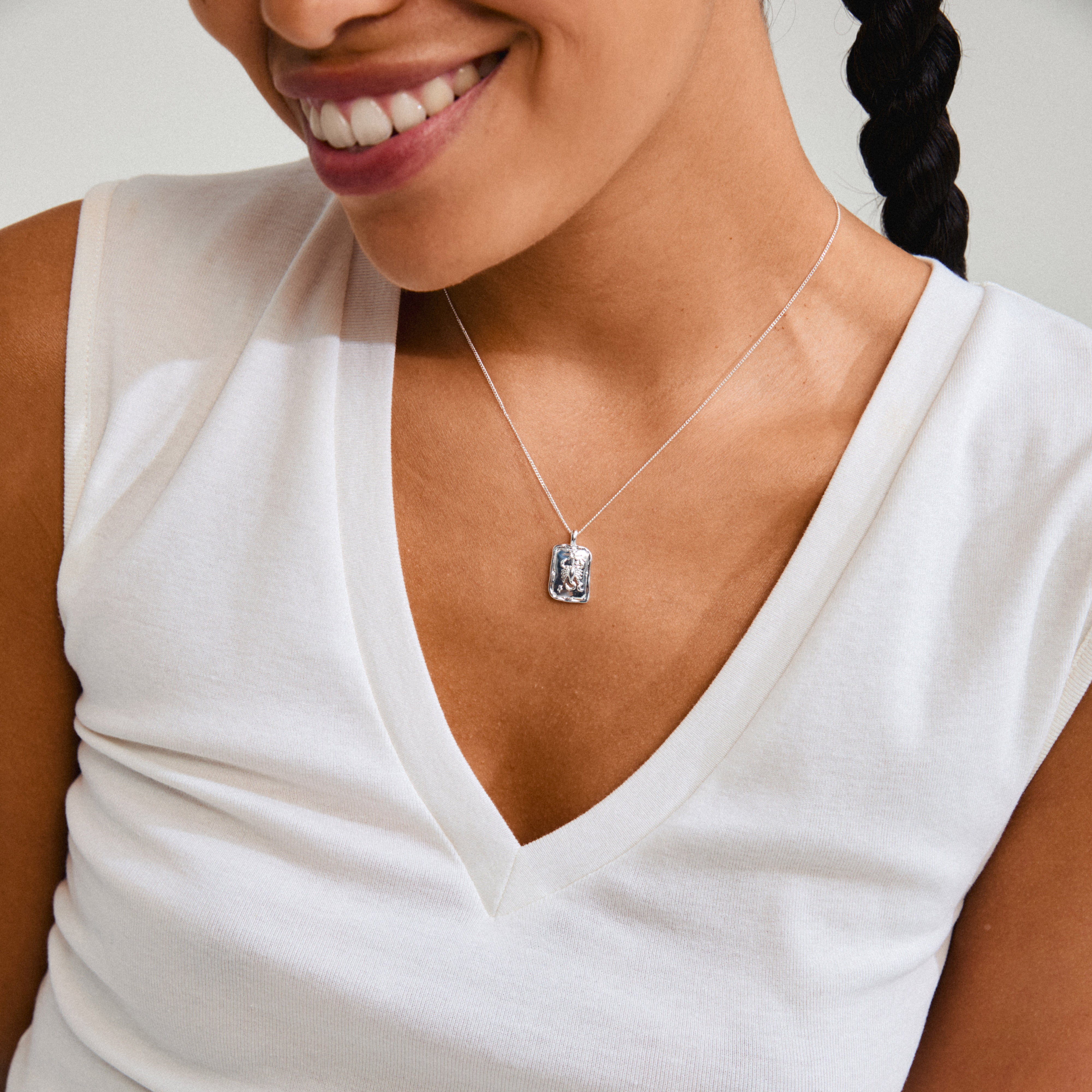 SCORPIO Zodiac Sign necklace, silver-plated, featuring a square coin pendant with a scorpion motif and sparkling constellation, worn by a smiling woman in a white shirt.