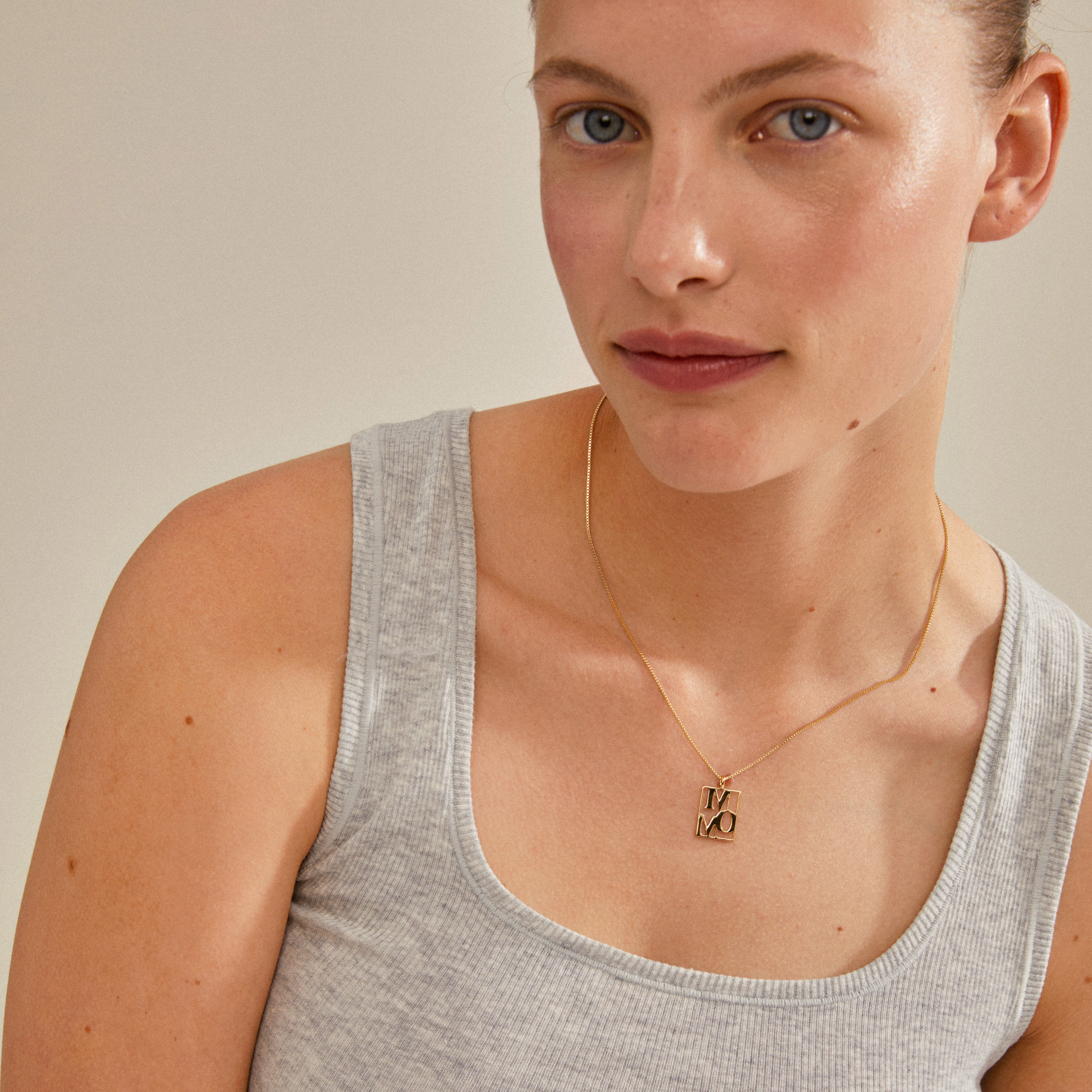 LOVE TAG, MOM necklace gold-plated, worn by a woman. Features a square pendant inscribed with MOM, offering an adjustable 40 cm chain with a 12 cm extension.
