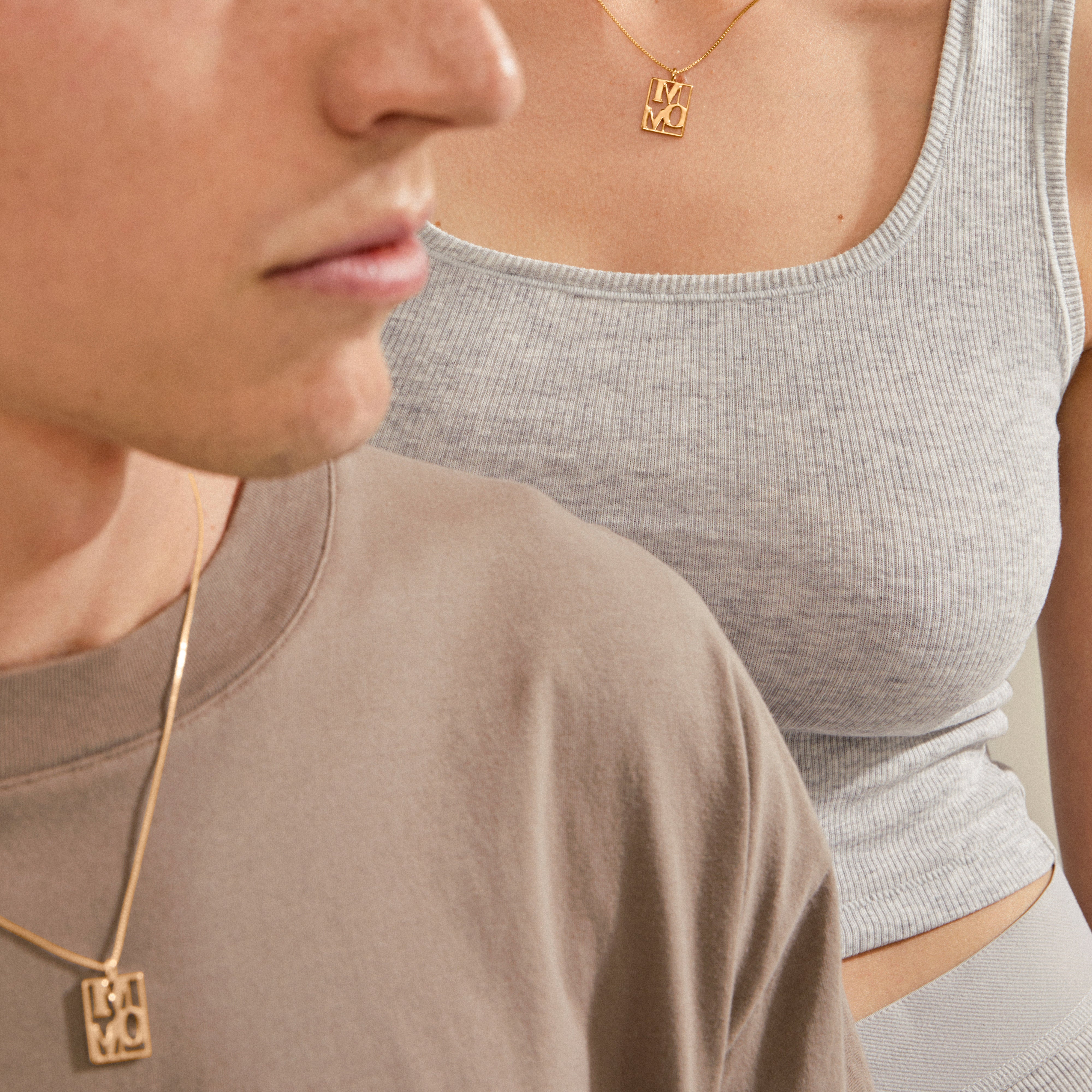 Close-up of two people wearing matching gold-plated LOVE TAG, MOM necklaces by Pilgrim, featuring square pendants spelling “MOMO,” showcasing a stylish, affectionate accessory.