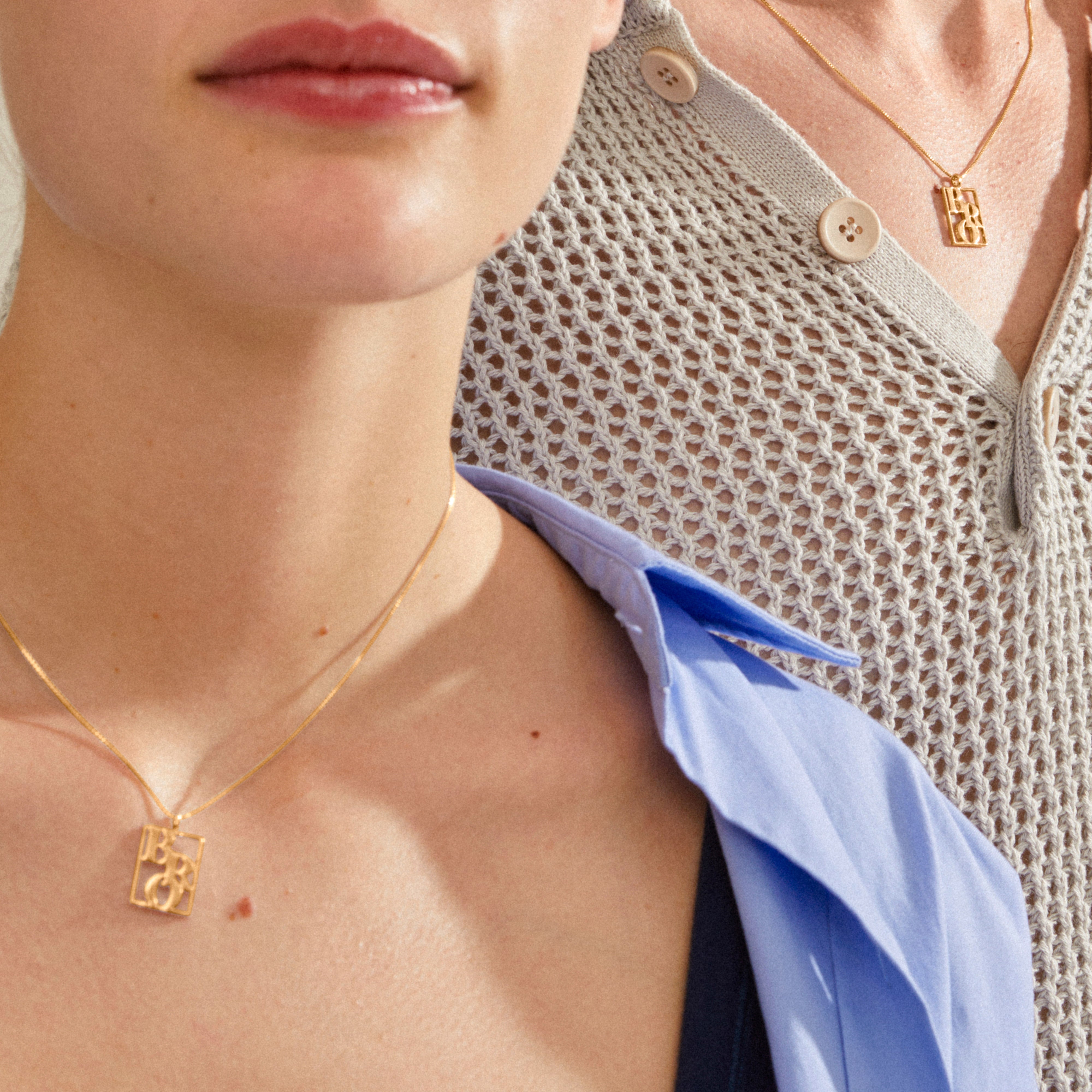 Two people wearing Pilgrim's LOVE TAG, BRO gold-plated necklaces with rectangular pendants, showcasing a trendy layered look against light blue and cream tops.