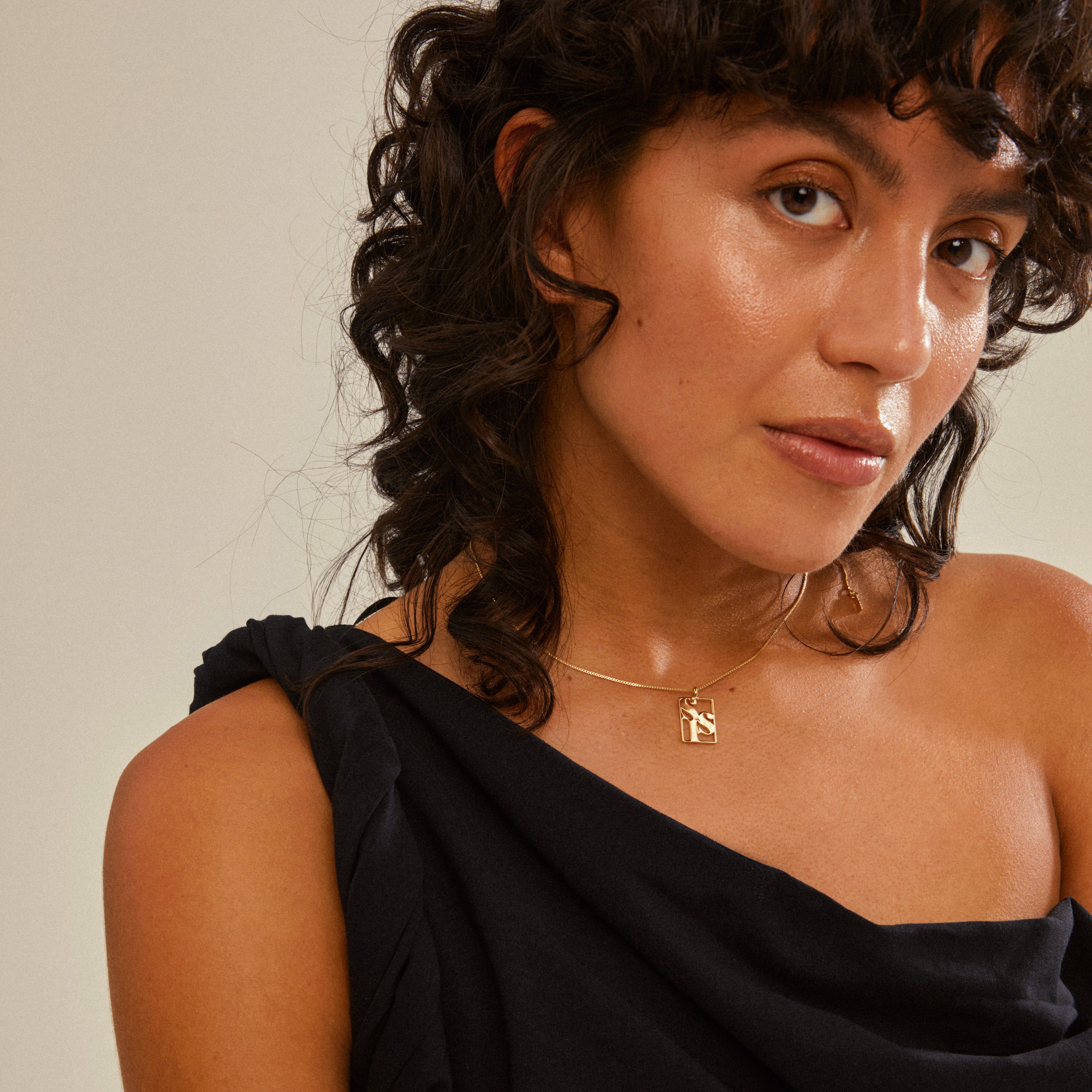 A woman wears the LOVE TAG, SIS gold-plated necklace featuring a square pendant. The chain is adjustable, perfect for layered styling.