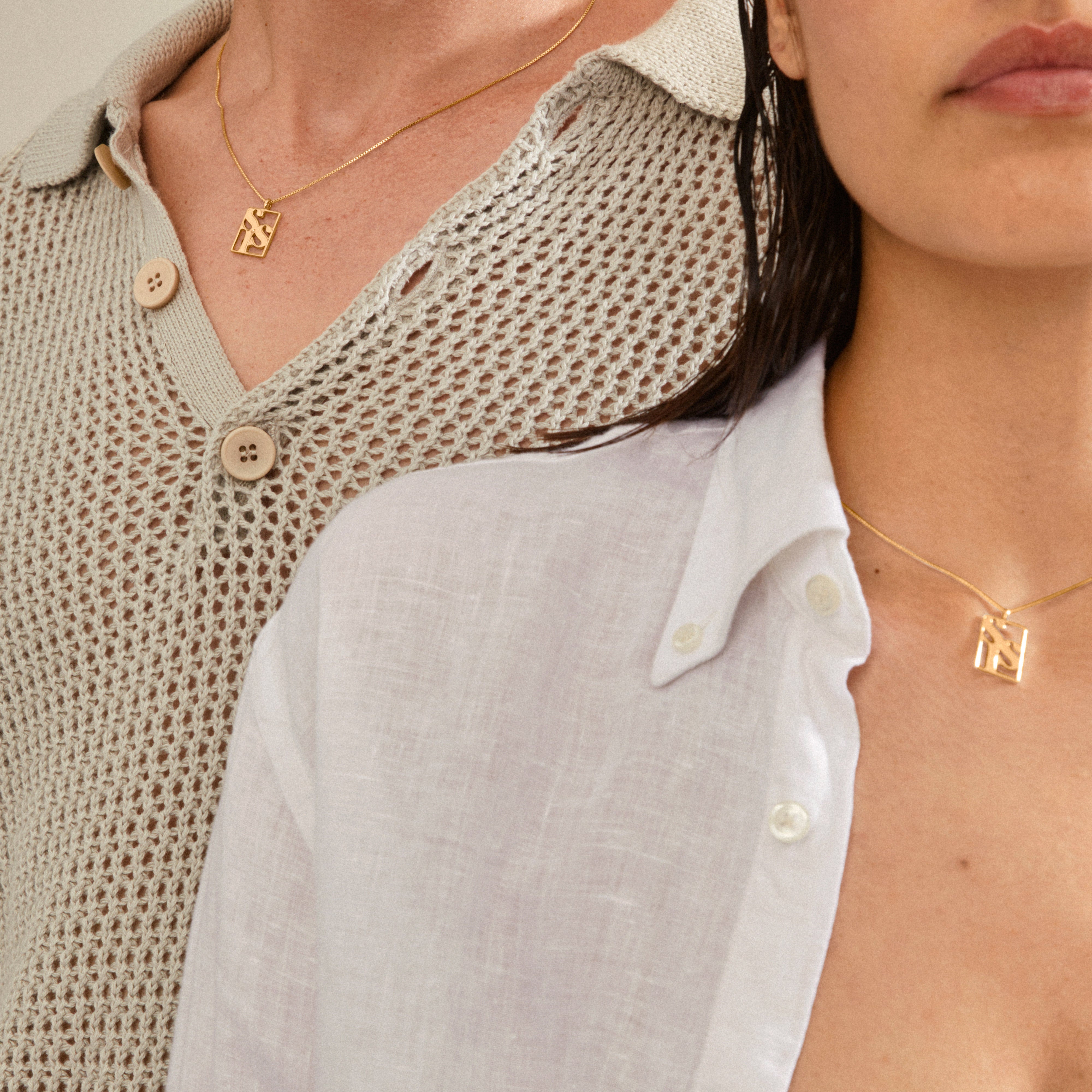 Two torsos wearing Pilgrim's gold-plated LOVE TAG, SIS necklaces, each featuring a square pendant with abstract cut-out design, highlighting minimalist elegance and Scandinavian craftsmanship.