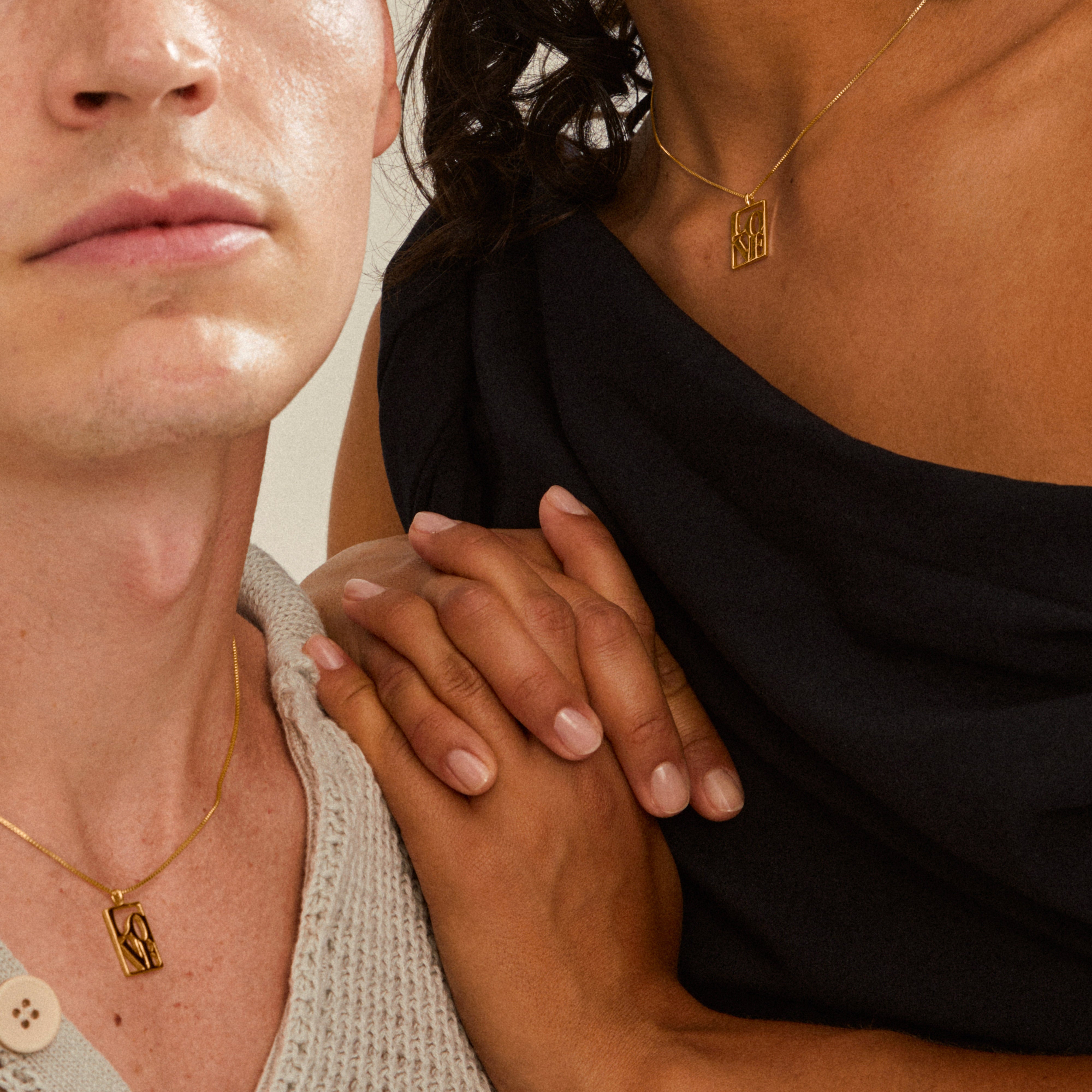 Two torsos wearing LOVE TAG gold-plated necklaces from Pilgrim, with small rectangular pendants spelling LOVE, emphasizing connection and style through layered, adjustable chains.