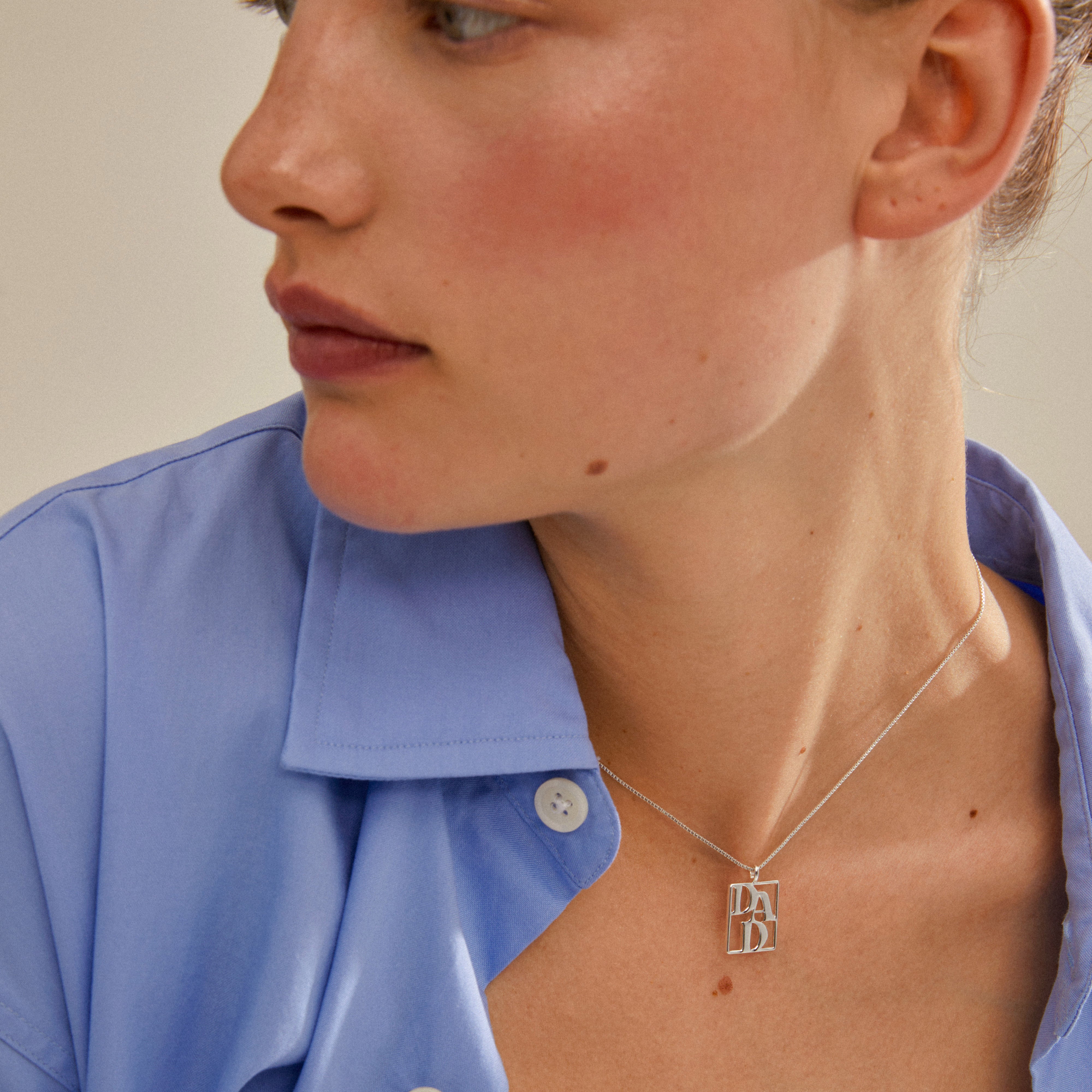 Woman wearing LOVE TAG, DAD necklace, silver-plated, with a square pendant inscribed with DAD, from Pilgrim's sustainable collection.
