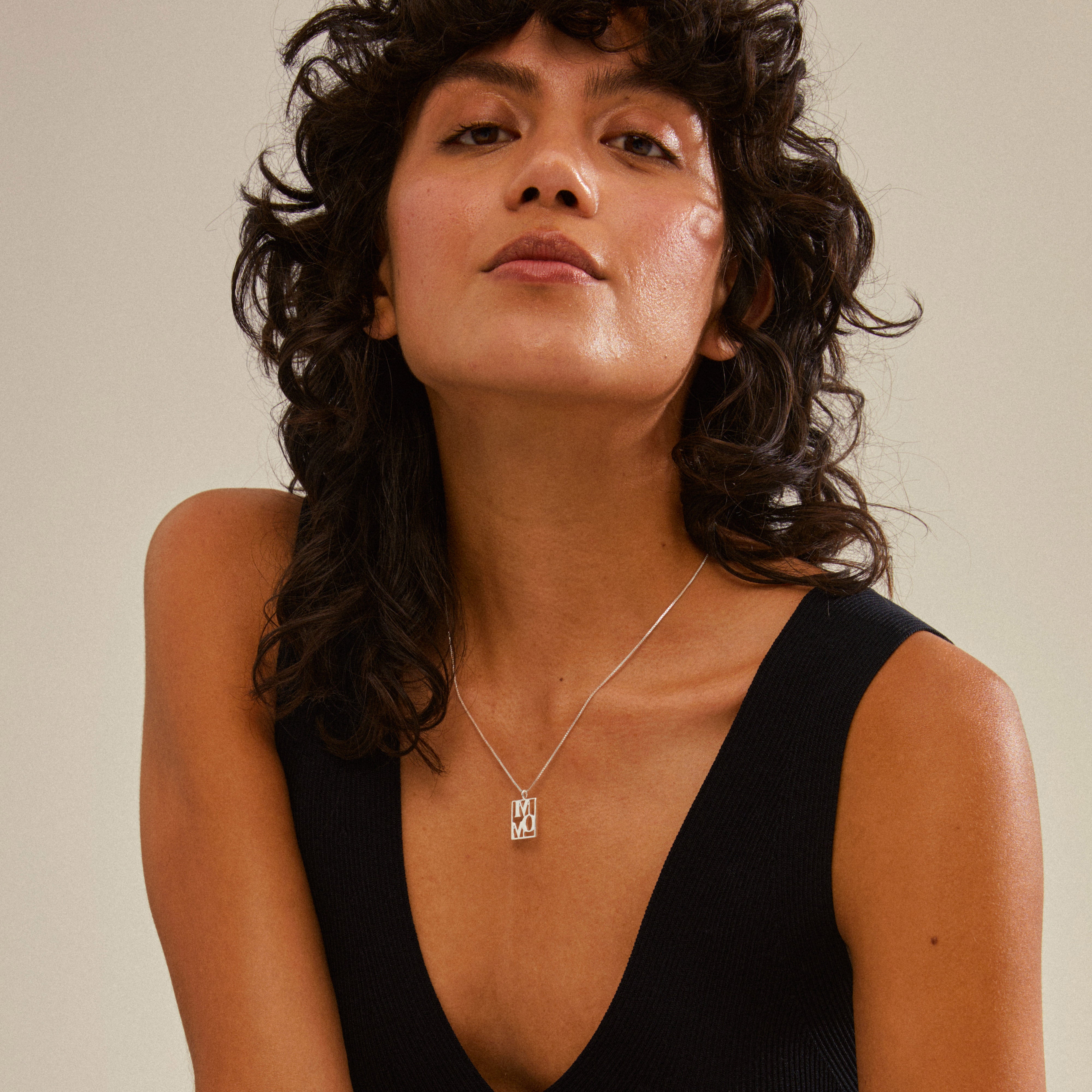 Woman with curly hair wearing a silver-plated LOVE TAG necklace, featuring a MOM pendant, showcasing Pilgrim's blend of timeless and trendy jewelry.