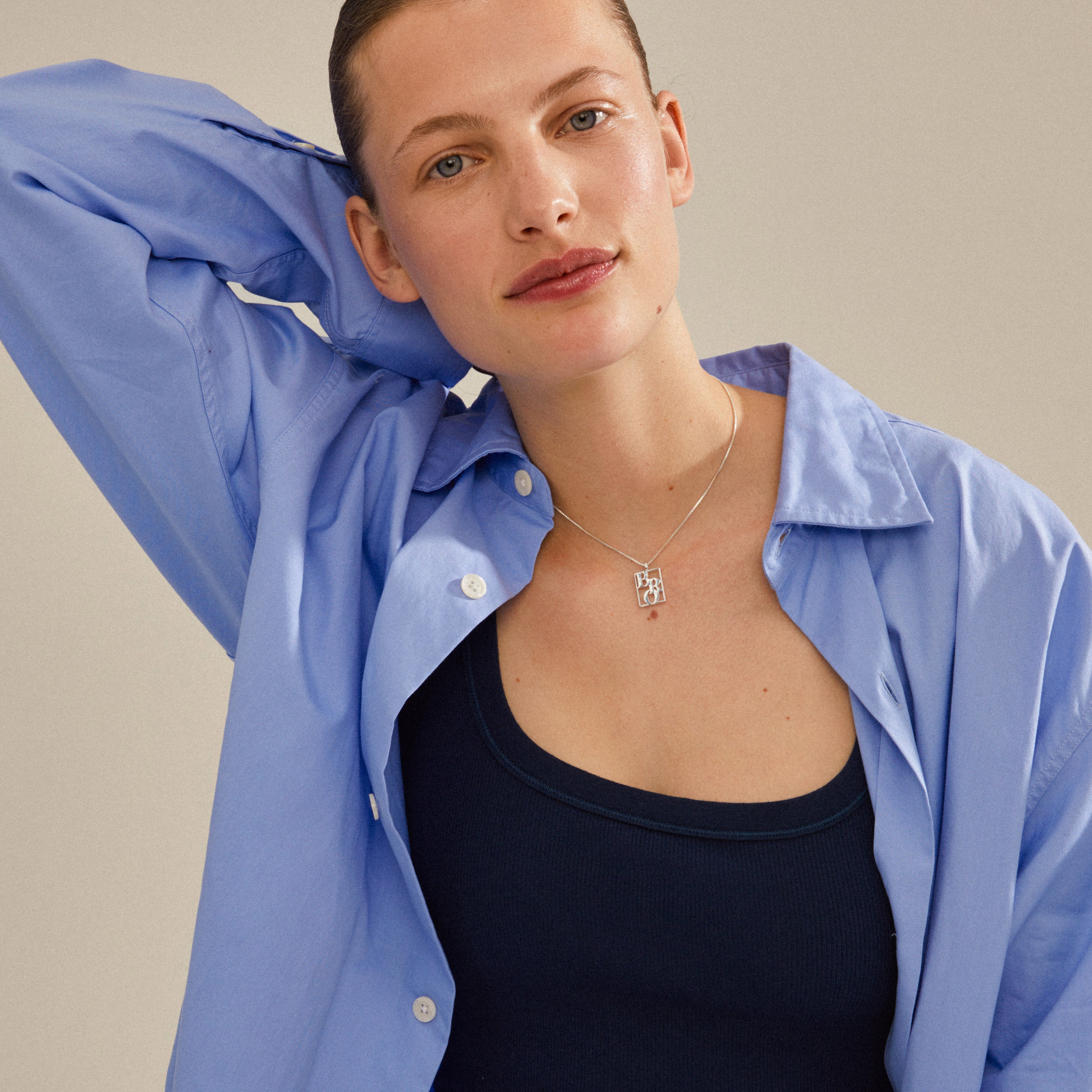 Woman showcasing a silver-plated LOVE TAG, BRO necklace from Pilgrim, featuring a square pendant inscribed with BRO on an adjustable chain.