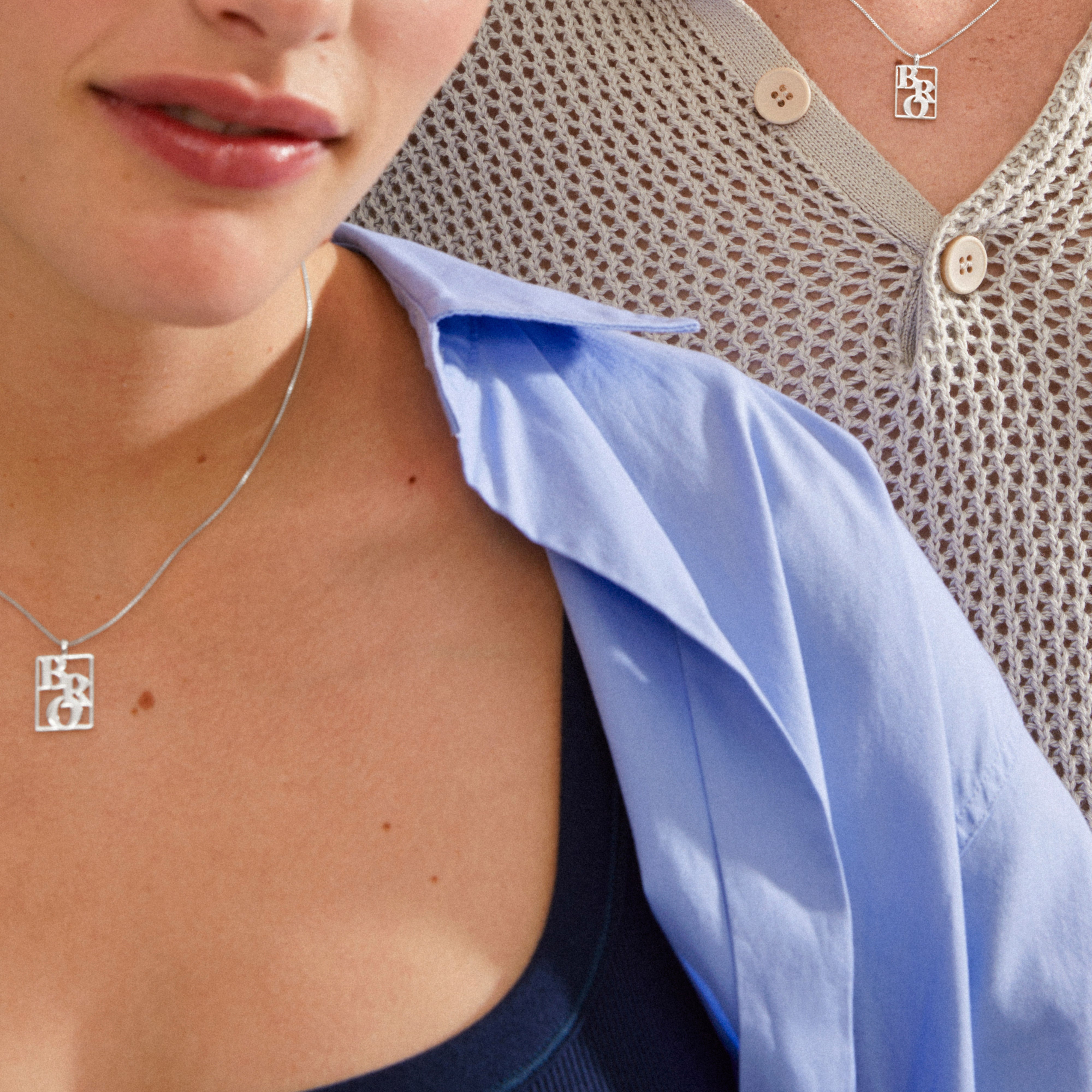 Two people wearing Pilgrim's LOVE TAG, BRO silver-plated necklaces, featuring a square pendant with BRO cut-out, showcasing stylish layering over casual outfits.