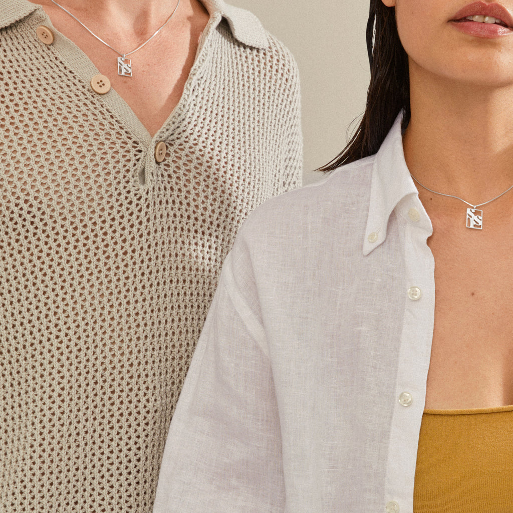 Two women showcase the LOVE TAG, SIS necklace, a silver-plated pendant with SIS on a delicate chain, embodying Pilgrim's blend of timeless and trendy jewelry.