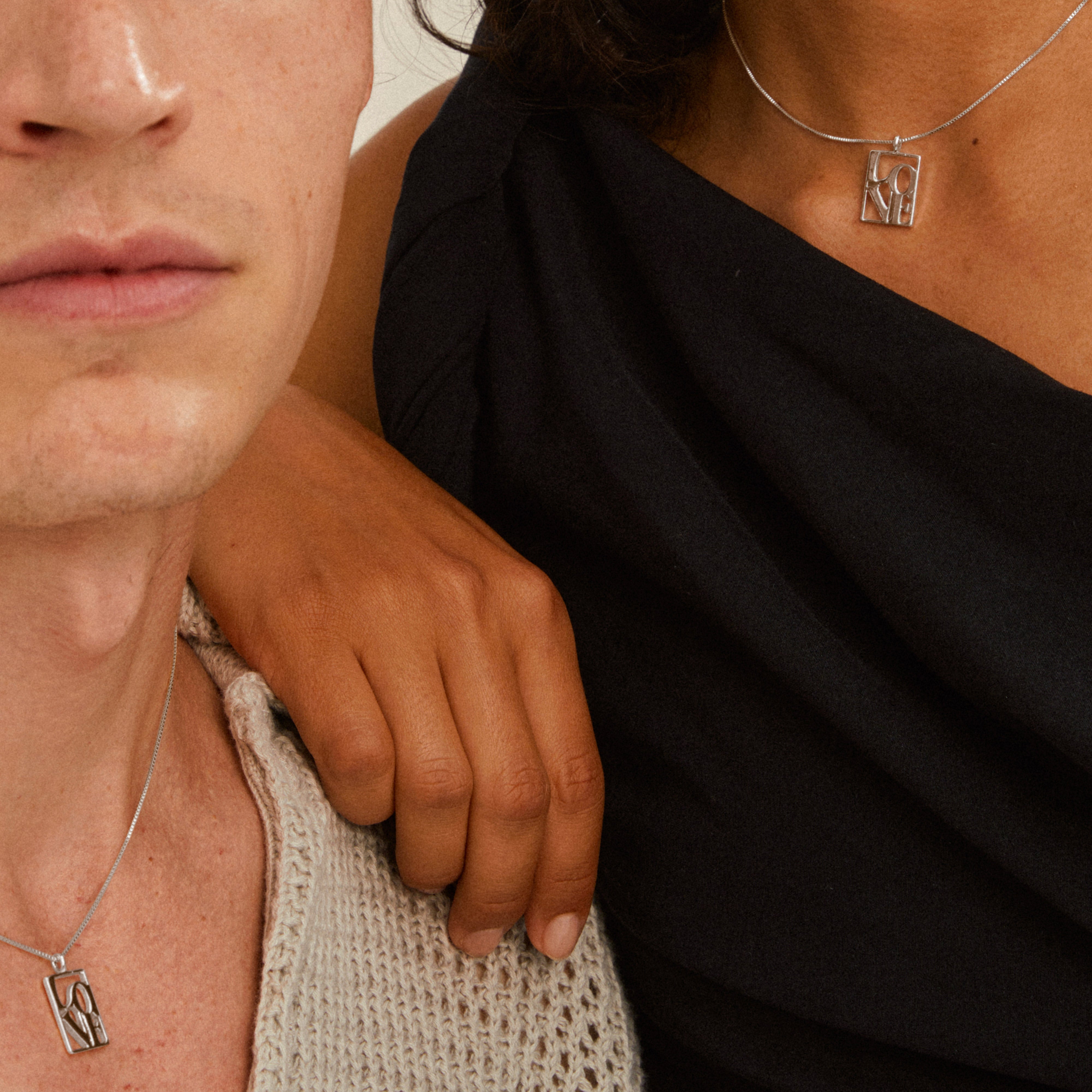 Two people wearing Pilgrim's LOVE TAG necklace, featuring a silver-plated chain with a rectangular pendant spelling LOVE in a modern cut-out design.