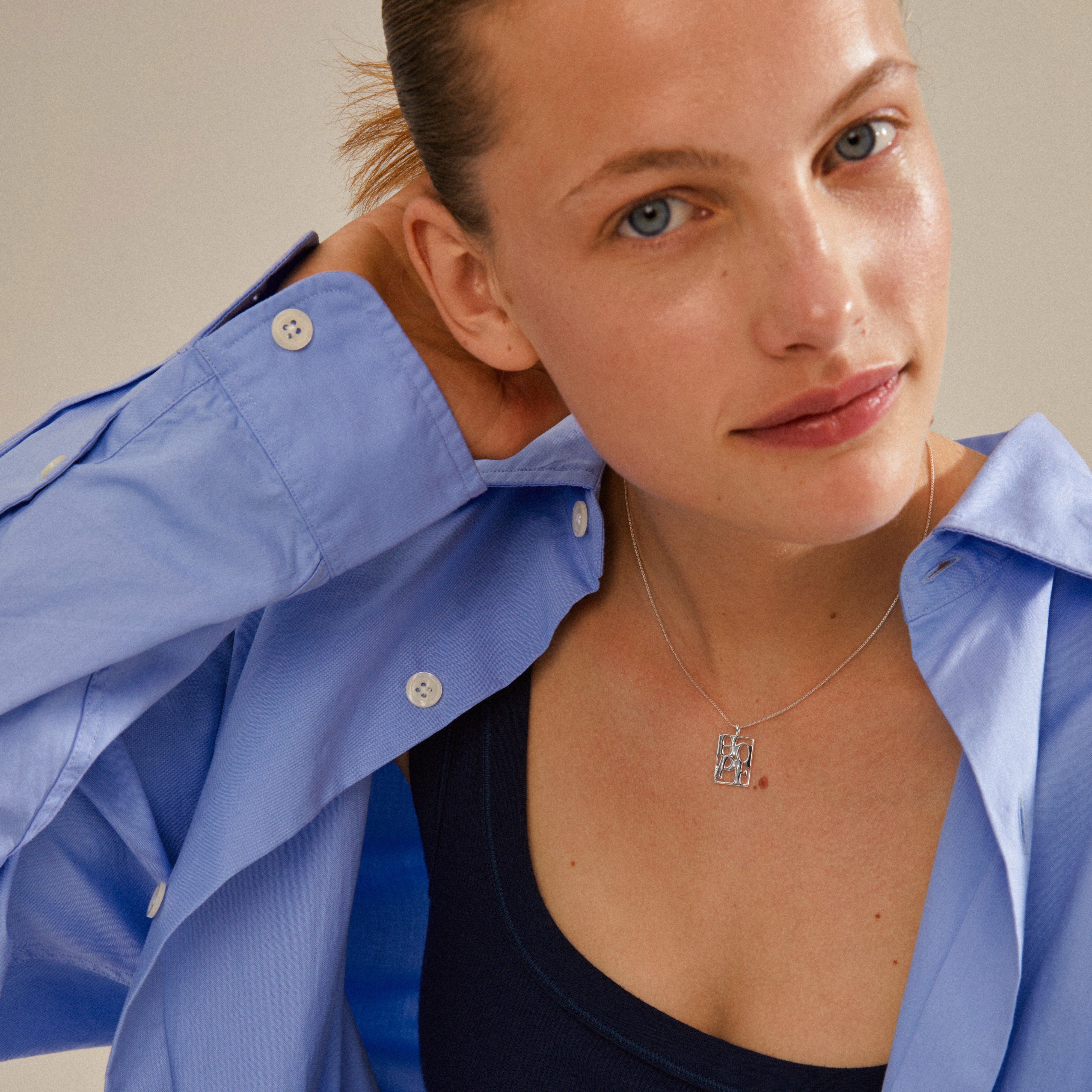 LOVE TAG, HOPE necklace silver-plated, featuring a square pendant with HOPE inscription, worn by a woman with her hand near her neck.