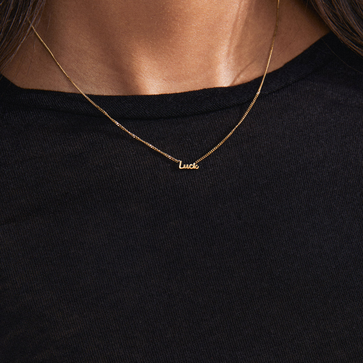 Gold-plated LUCK necklace with a cursive script pendant, worn by a person. A versatile, genderless accessory perfect for layering and personal styling.