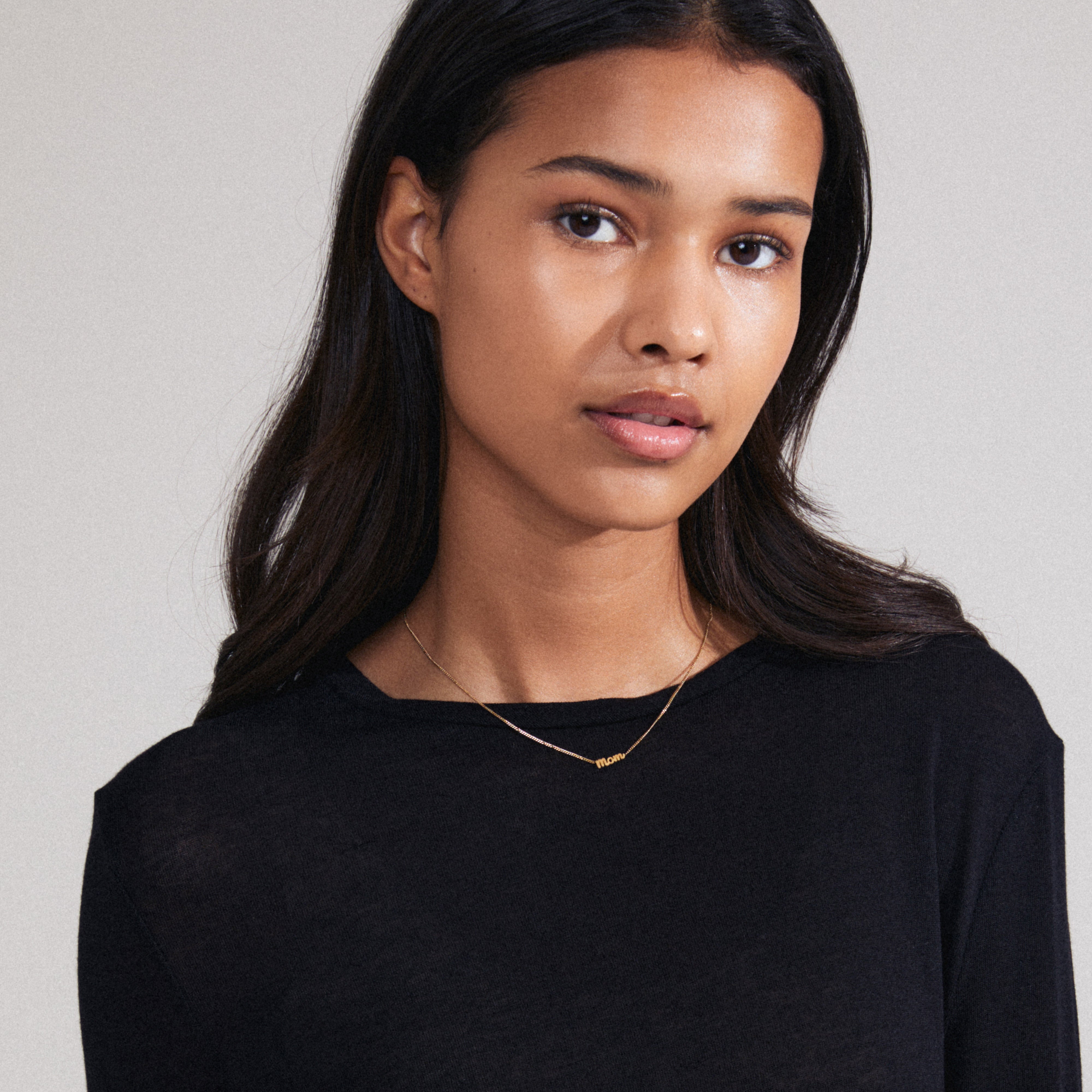 Gold-plated MOM necklace with cursive pendant, worn by woman in black shirt; a versatile gift made from 99% recycled materials.