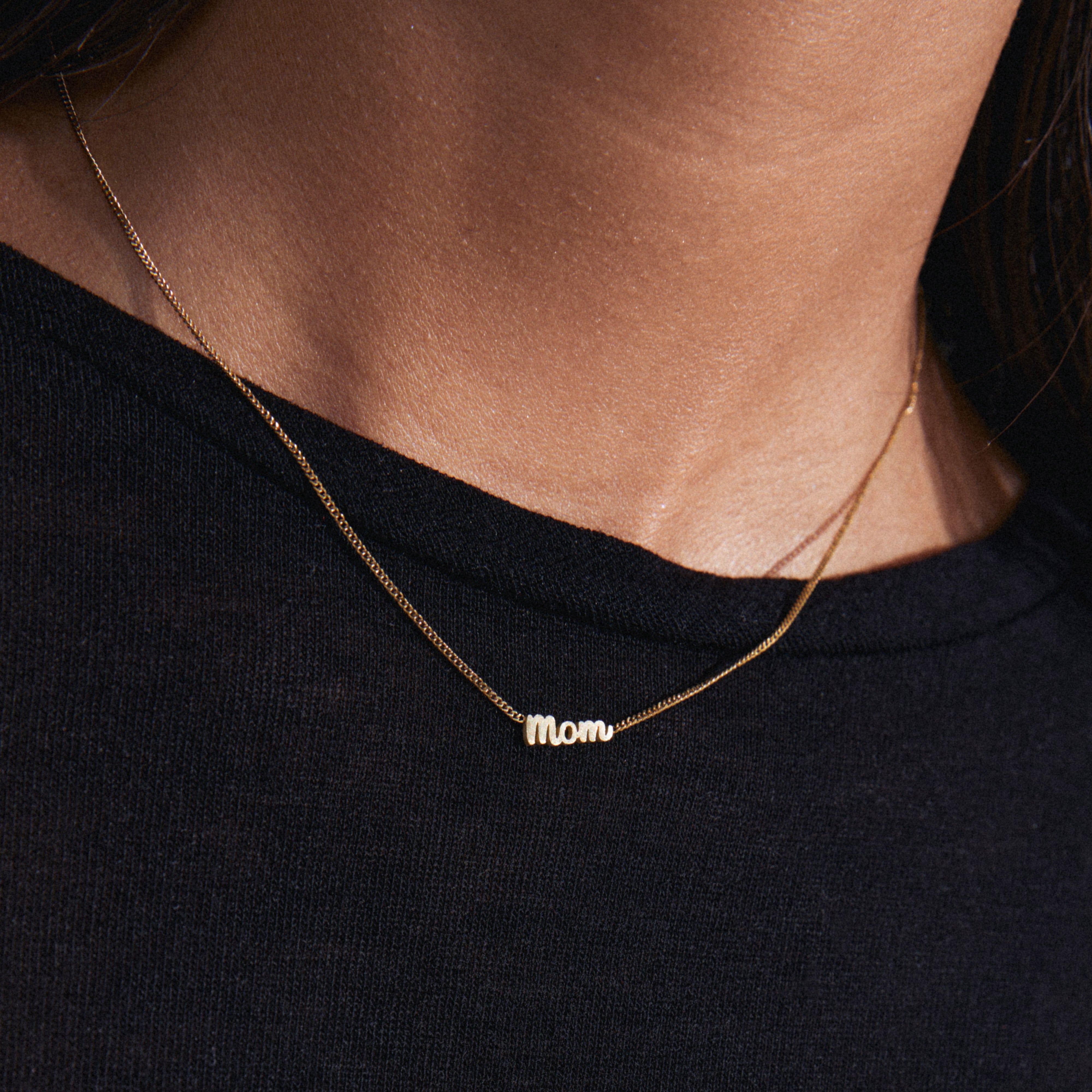 Gold-plated MOM necklace featuring a sleek, cursive pendant, worn by a person, highlighting a timeless, genderless design from Pilgrim's collection.
