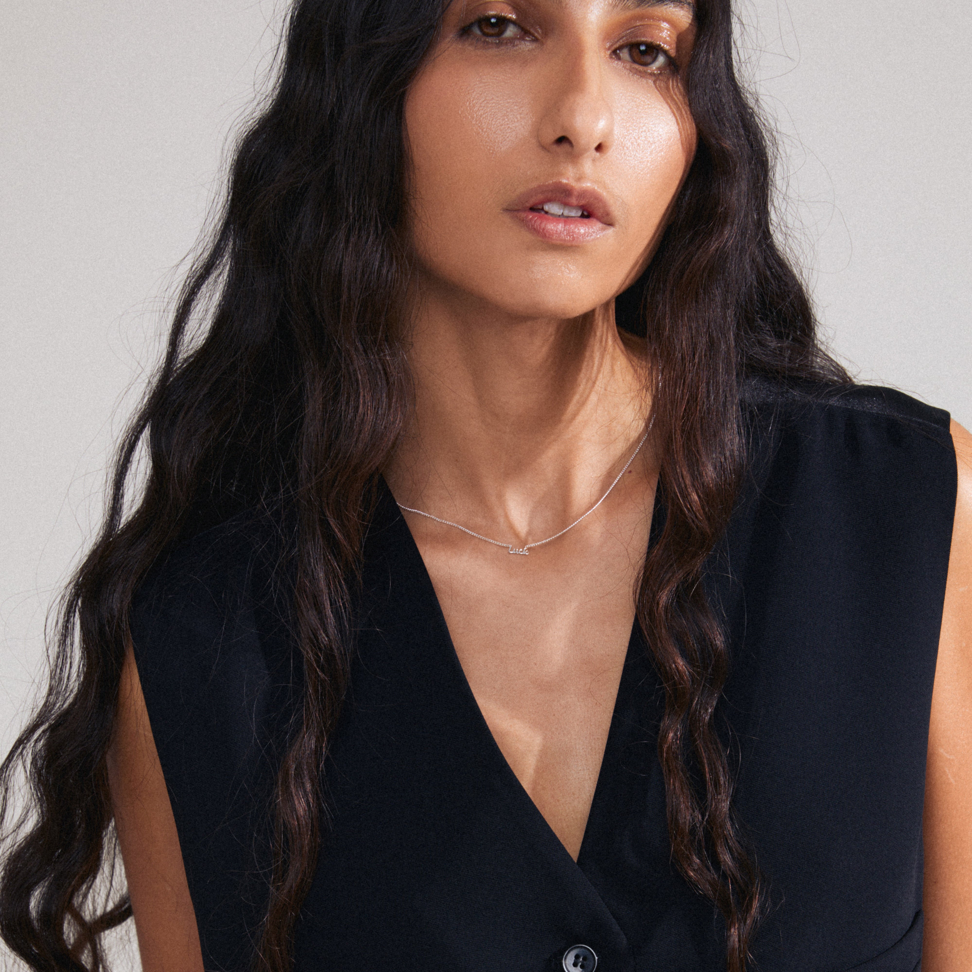 Woman wearing the LUCK necklace, a silver-plated piece with a cursive 'LUCK' pendant, showcasing a sleek, genderless design ideal for layering and everyday wear.