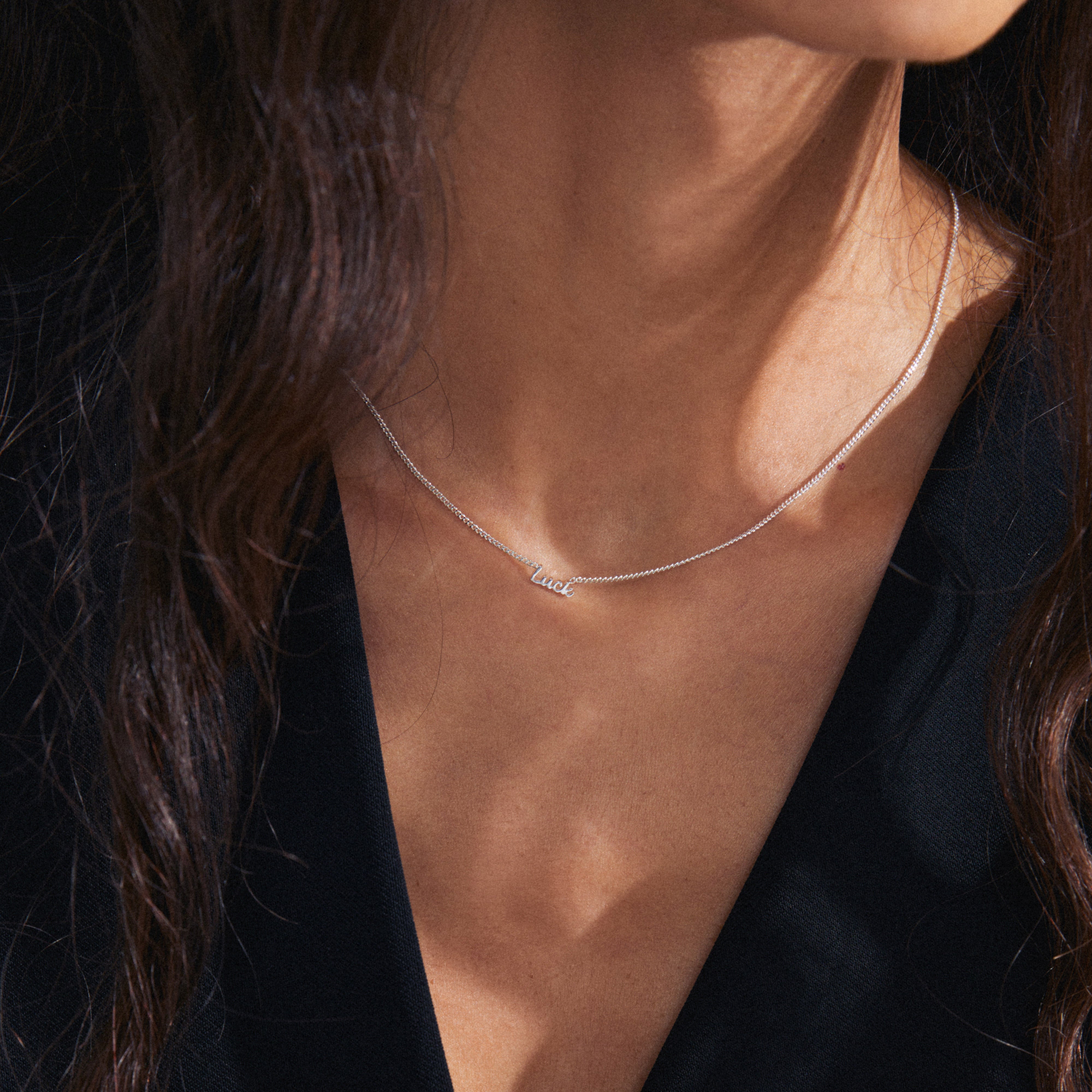 Woman wears LUCK silver-plated necklace with cursive pendant, showcasing sleek design and eco-friendly craftsmanship. Ideal for layering or solo wear, perfect for personal style.