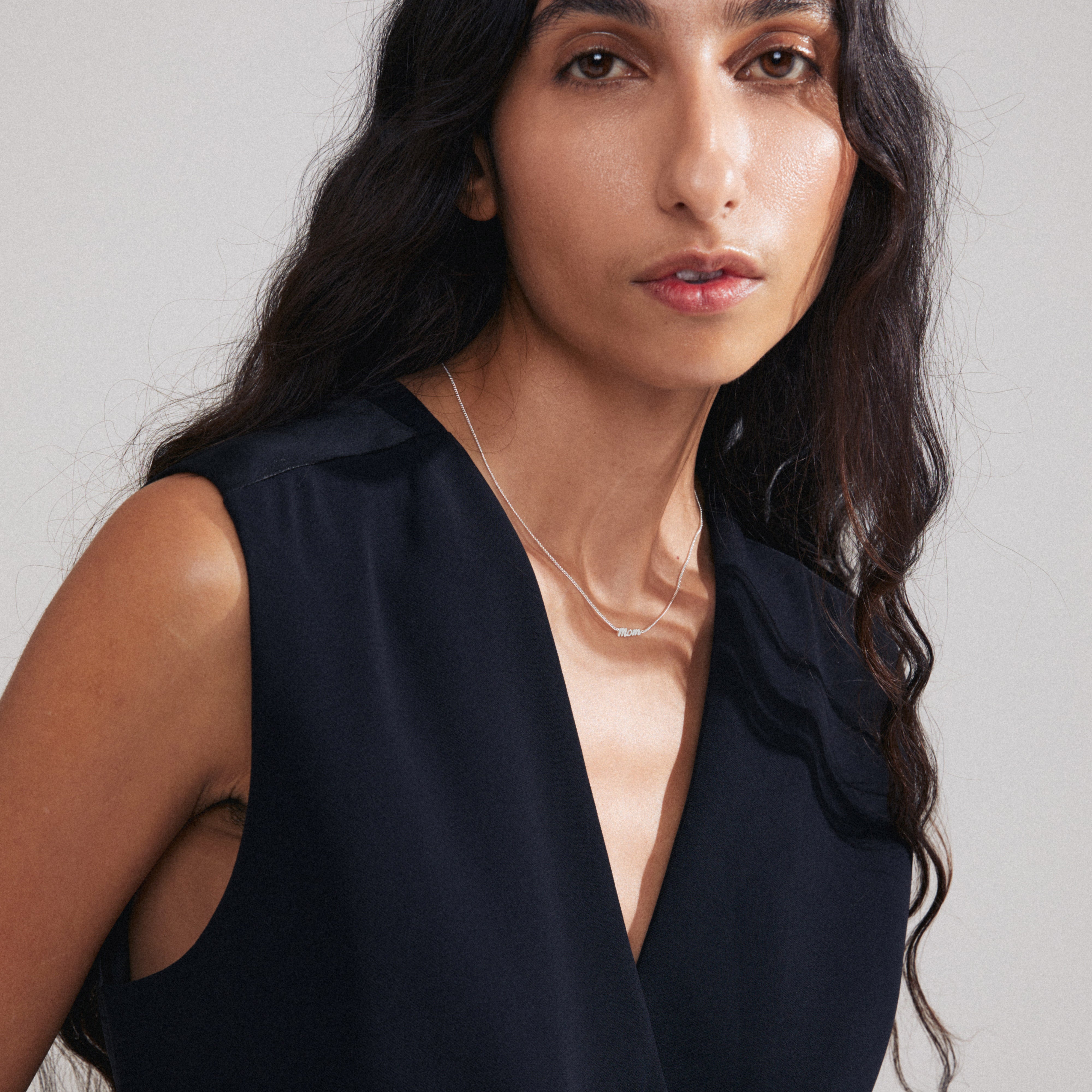 MOM necklace silver-plated, featuring a sleek cursive pendant, worn by a woman with long hair, showcasing a trendy, recycled design for daily wear.