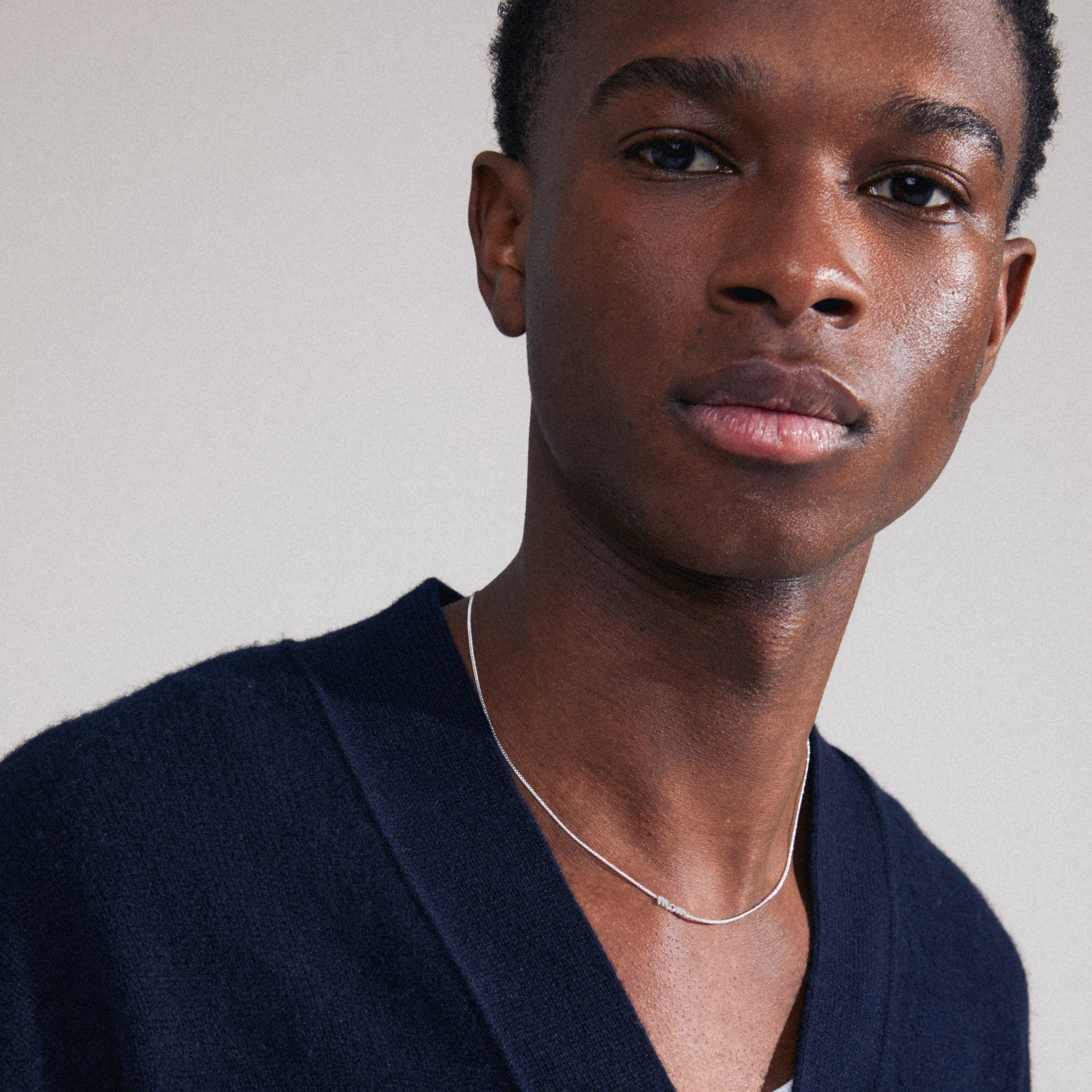 Silver-plated MOM necklace with a cursive pendant, worn by a man in a blue sweater, highlighting its genderless design and personalized elegance.