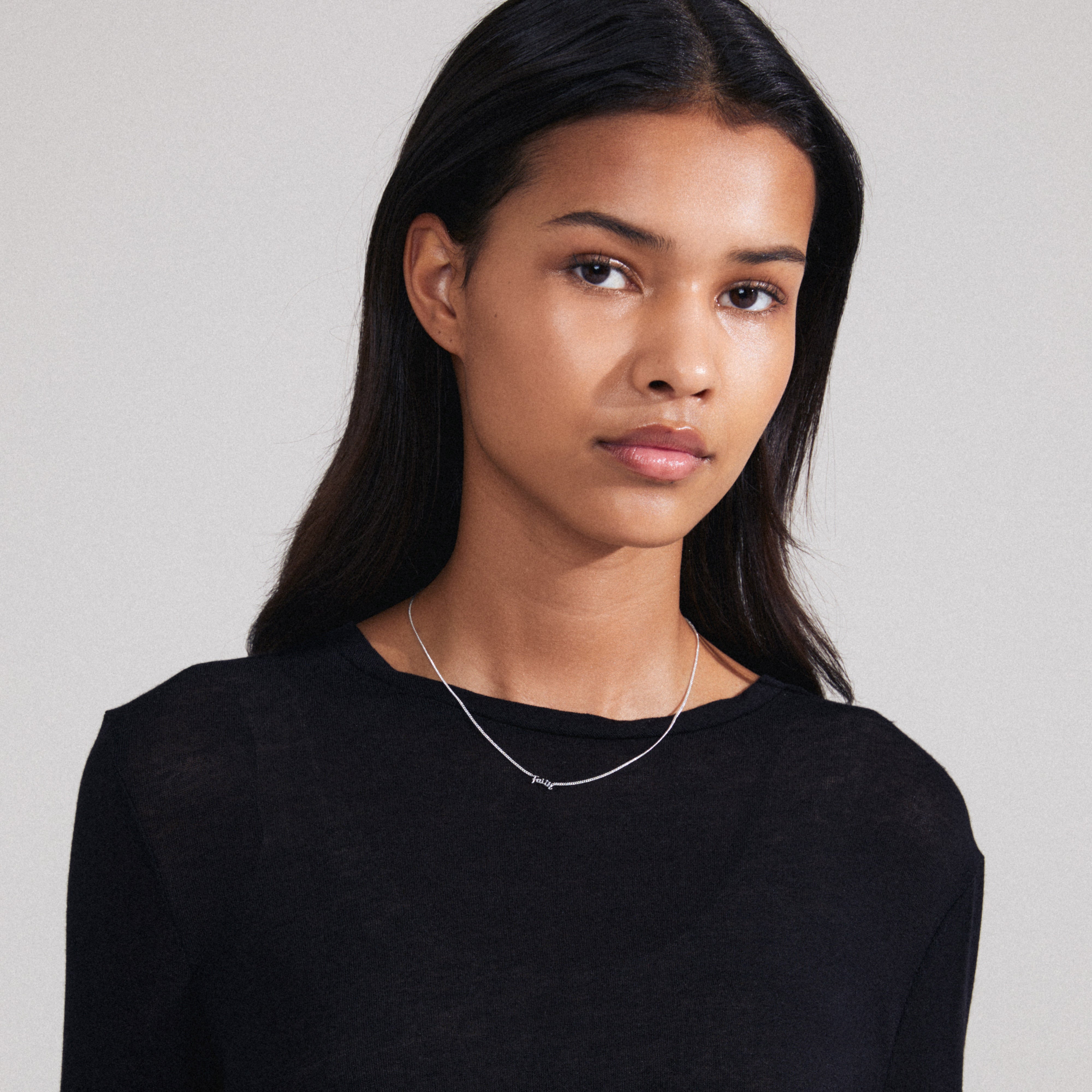 FAITH necklace, silver-plated, worn by a woman. Features a cursive 'FAITH' pendant, ideal for daily wear, crafted mainly from recycled materials.