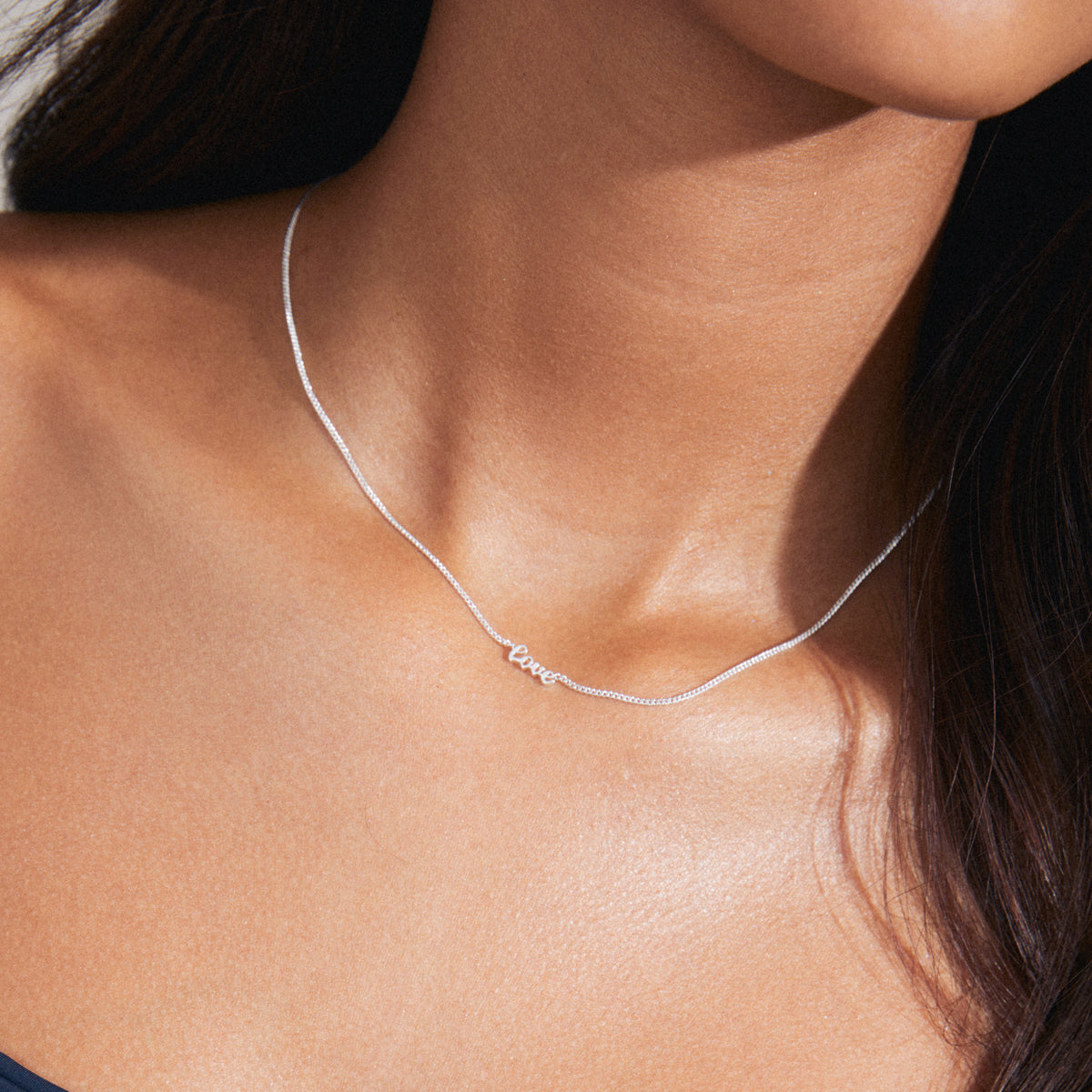 Woman wearing the LOVE necklace, a sleek silver-plated piece with a cursive 'LOVE' pendant, embodying personal style and inclusivity.