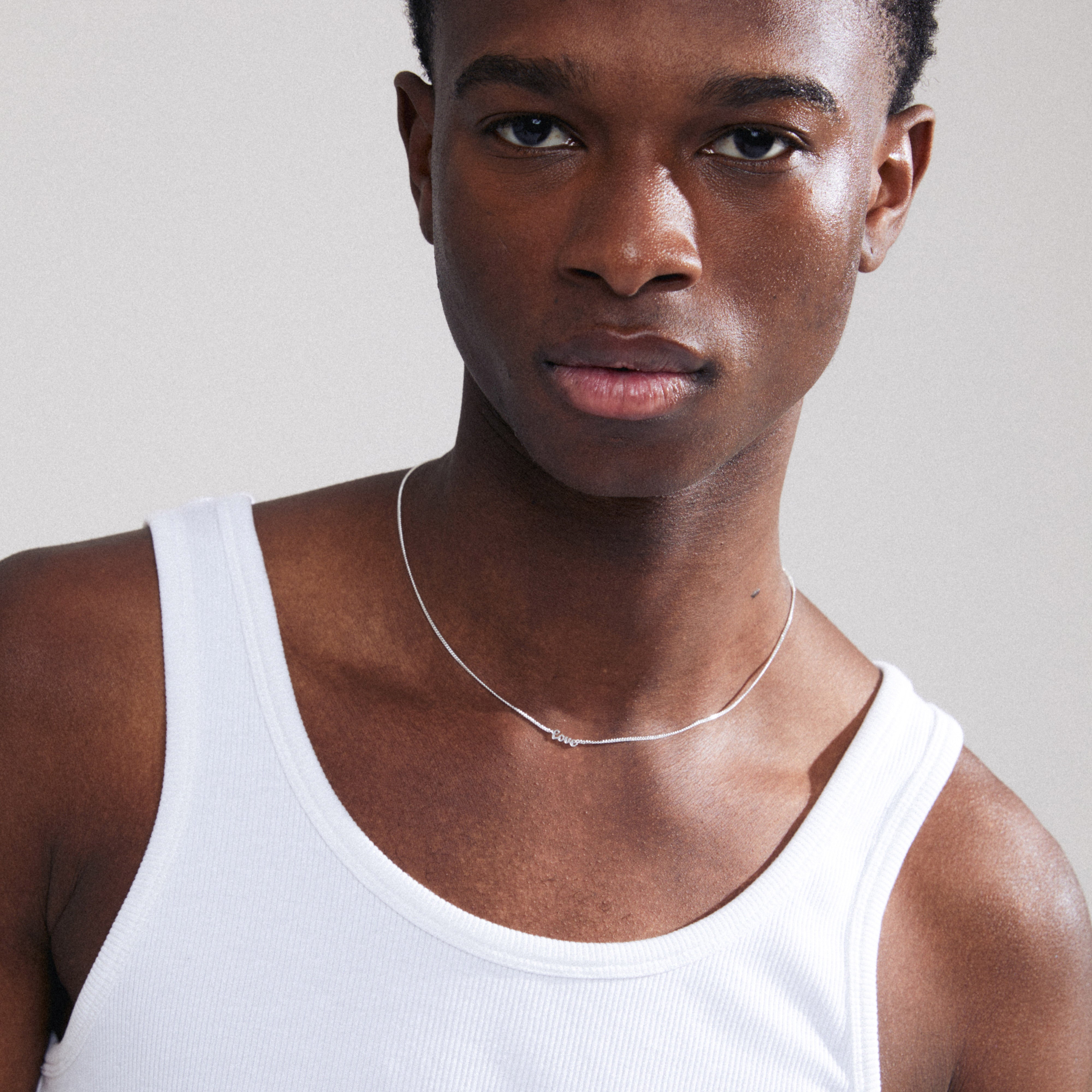 LOVE necklace silver-plated on a man in a white tank top, showcasing a sleek, cursive 'LOVE' pendant, perfect for personal style and everyday wear.