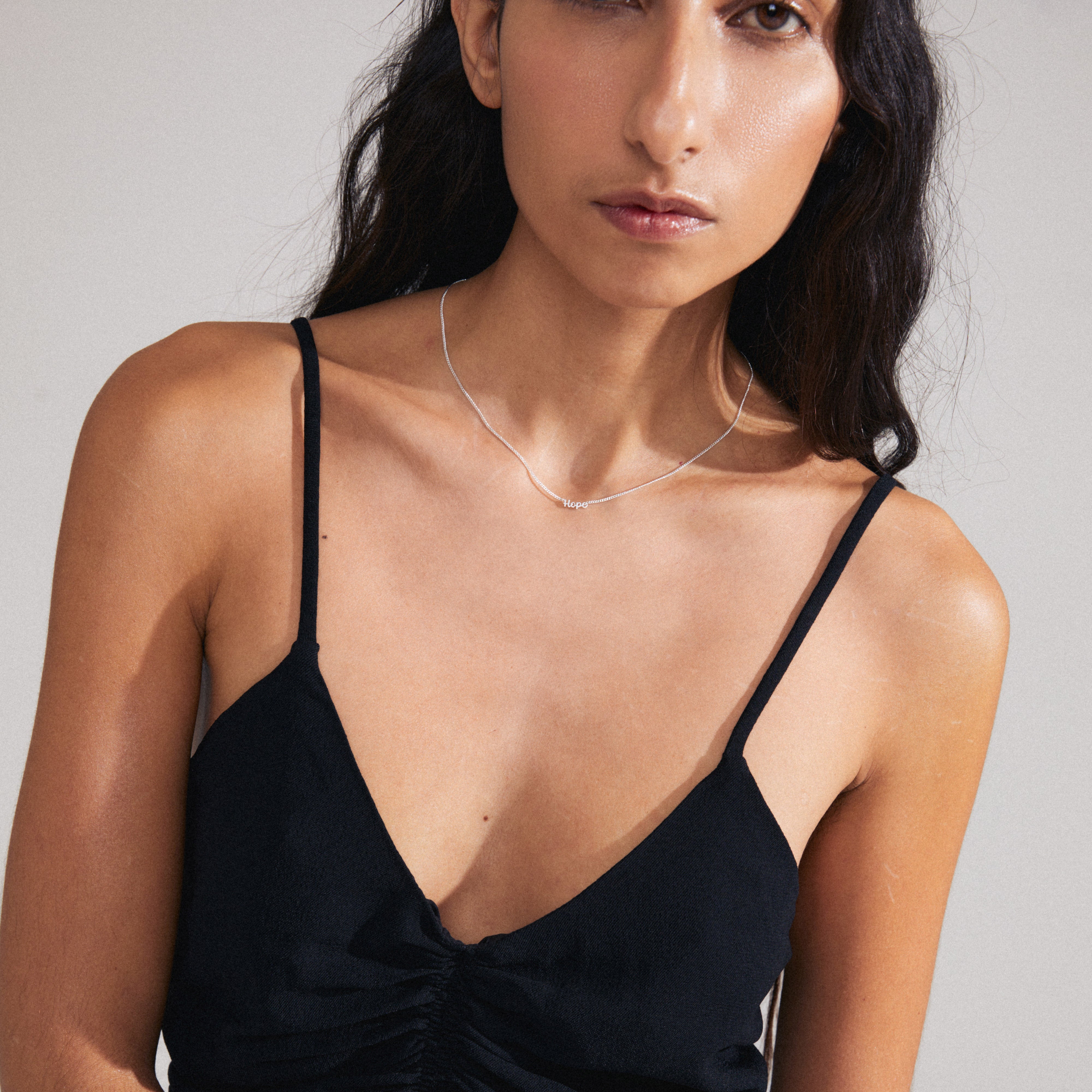 Woman wearing HOPE necklace, a sleek silver-plated pendant with 'HOPE' in cursive, layered on her chest, representing personal style and inclusivity.