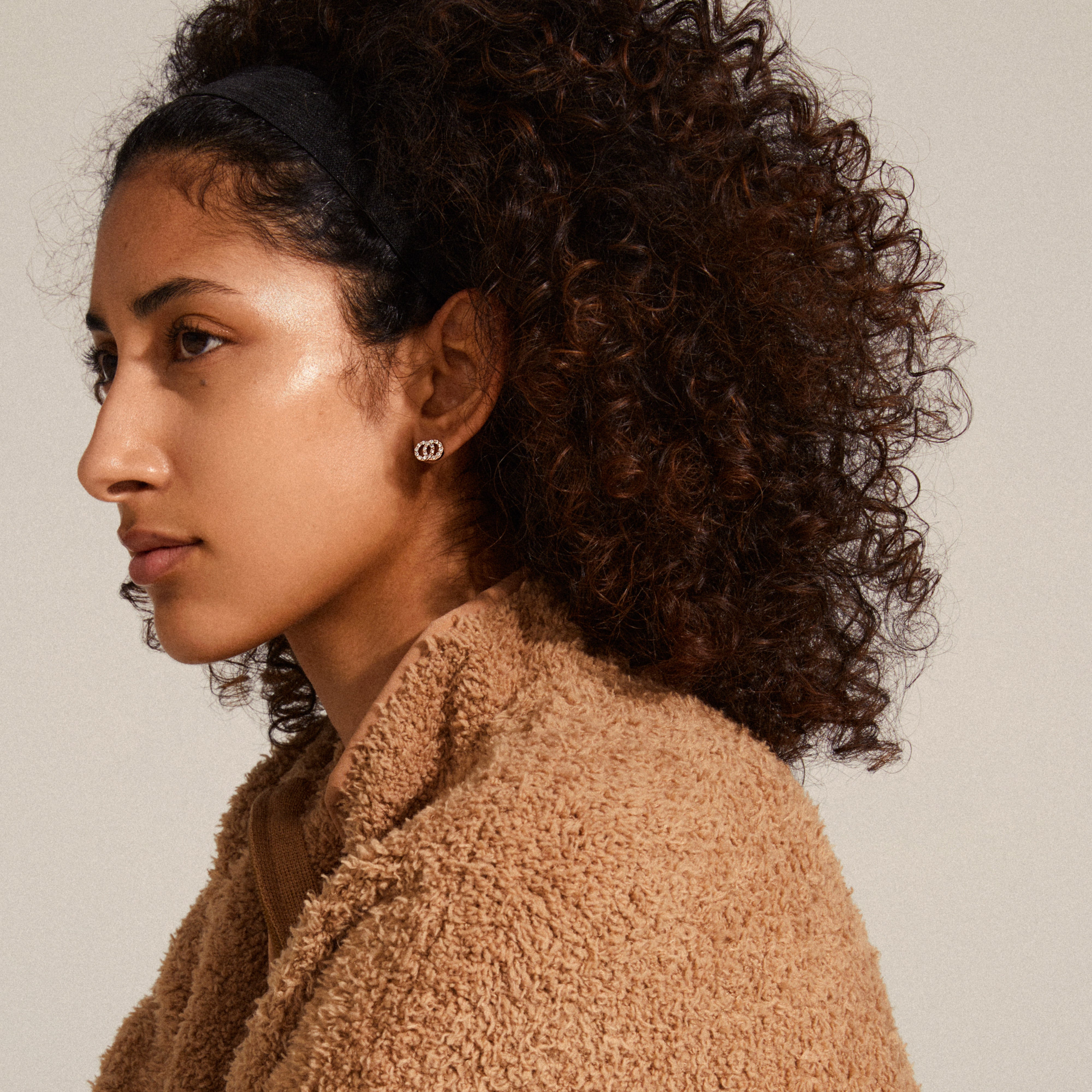 VICTORIA crystal earrings in rose gold, shaped as intertwined rings with bright crystals, worn by a woman with curly hair, showcasing elegant Pilgrim style.