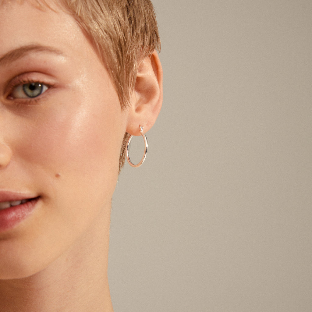 LAYLA medium hoop earrings, silver-plated, adorn a woman's ear, highlighting their elegant, timeless design and easy click clasp. Perfect for any stylish ensemble.