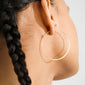 Close-up of TILLY large gold-plated hoop earring adorning an ear with a long dark braid, embodying sleek Scandinavian style from Pilgrim.
