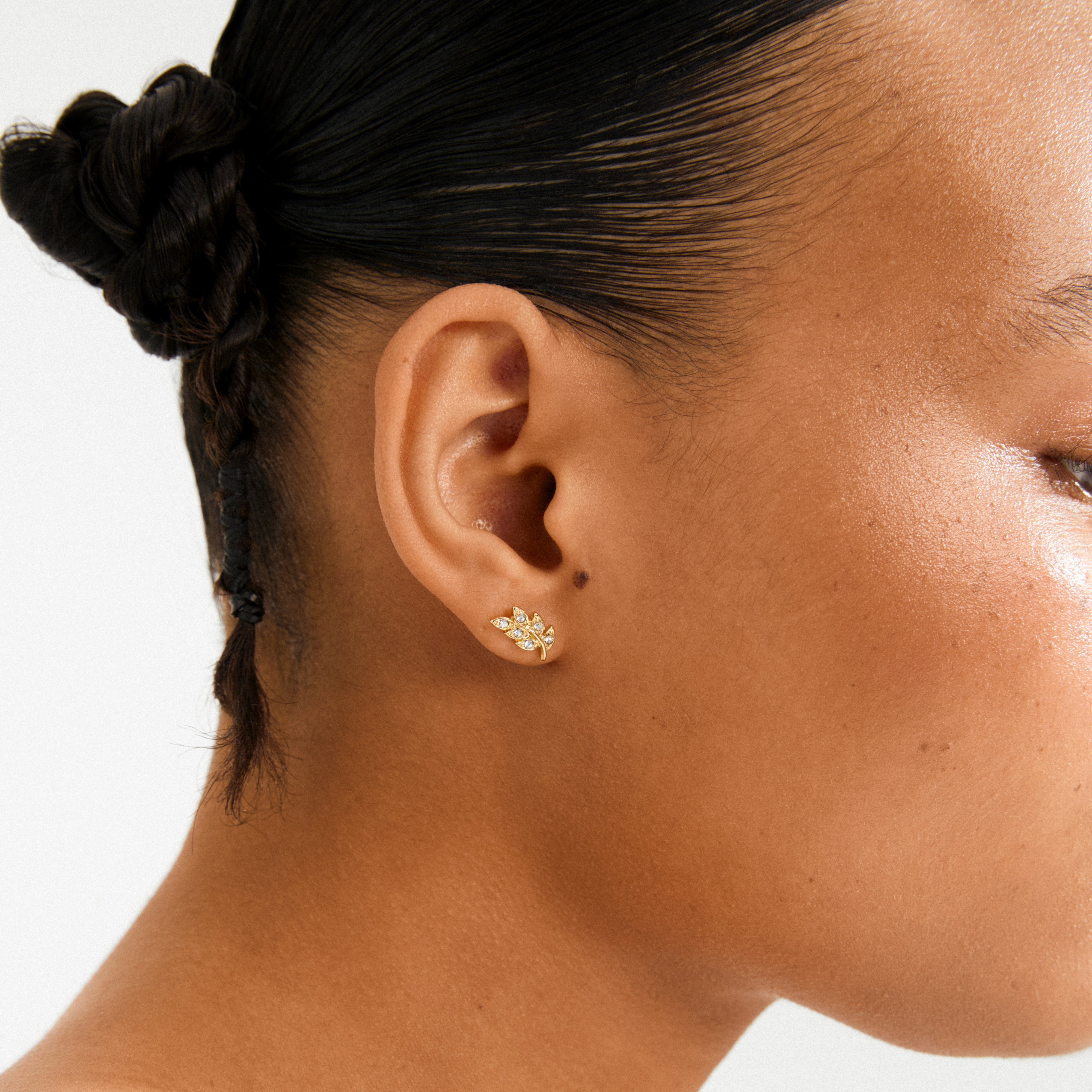 Close-up of an ear wearing Pilgrim's IMOGEN crystal leaf earrings, gold-plated with tiny sparkling crystals, showcasing elegant nature-inspired design.