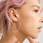 Side profile of a person wearing Pilgrim's TILLY large silver-plated hoop earring, showcasing its sleek, airy design. Hand lightly touching chin, emphasizing minimalist style.