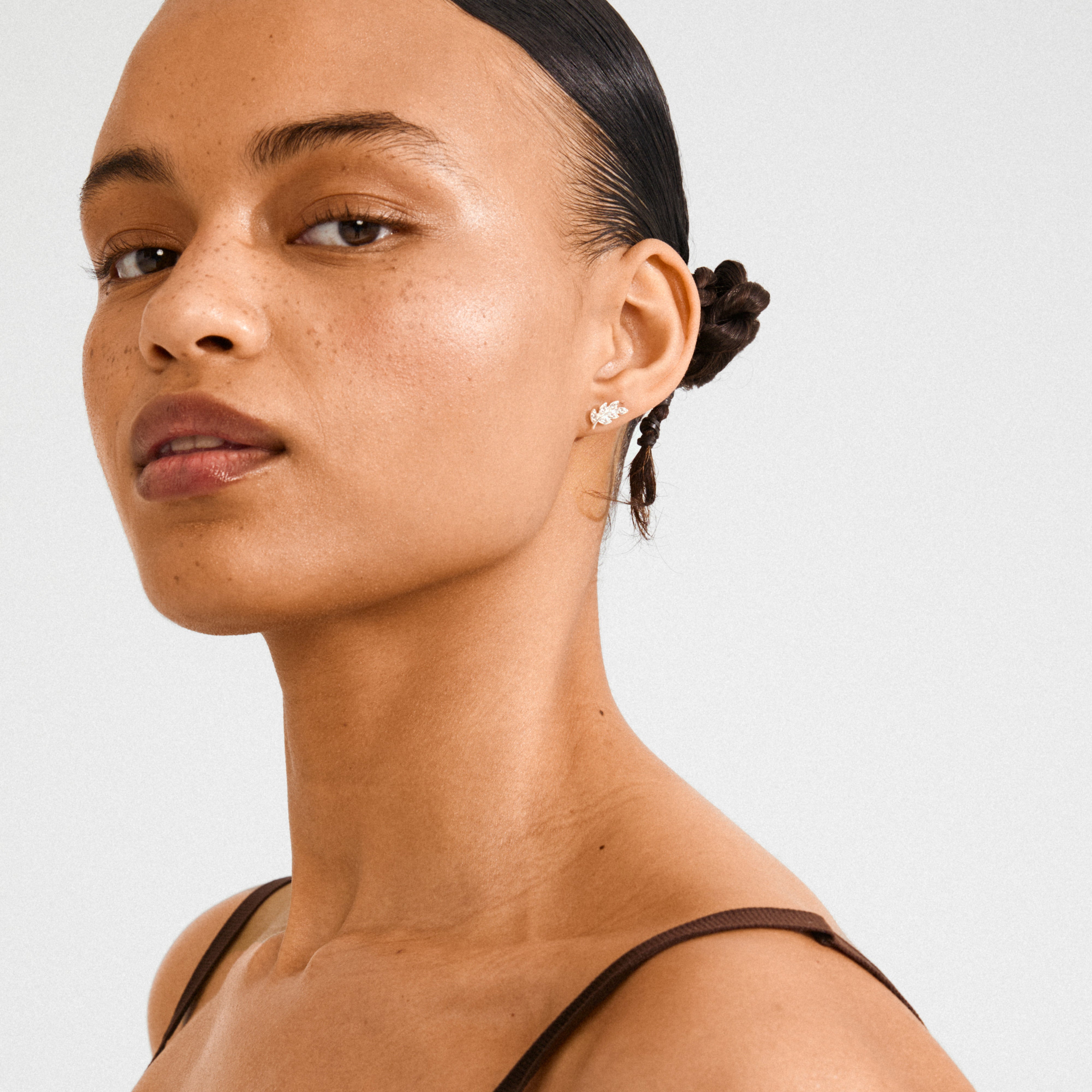 Young woman wearing Pilgrim's IMOGEN crystal leaf earrings, silver-plated, capturing light with delicate sparkling crystals, highlighting nature-inspired elegance and style.