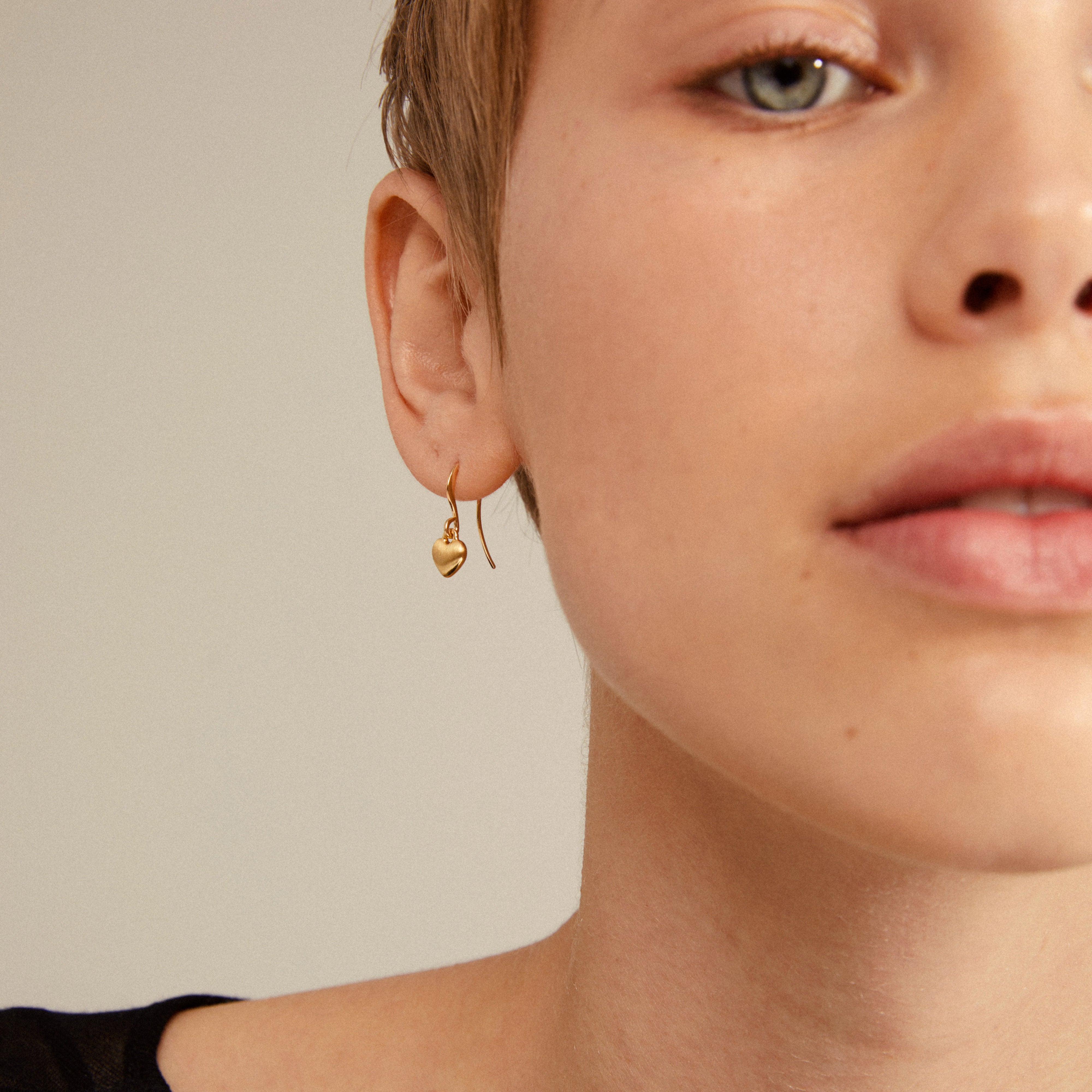 SOPHIA heart pendant earrings gold-plated, shown as a stylish accessory on a woman's ear, ideal for both everyday and evening wear.