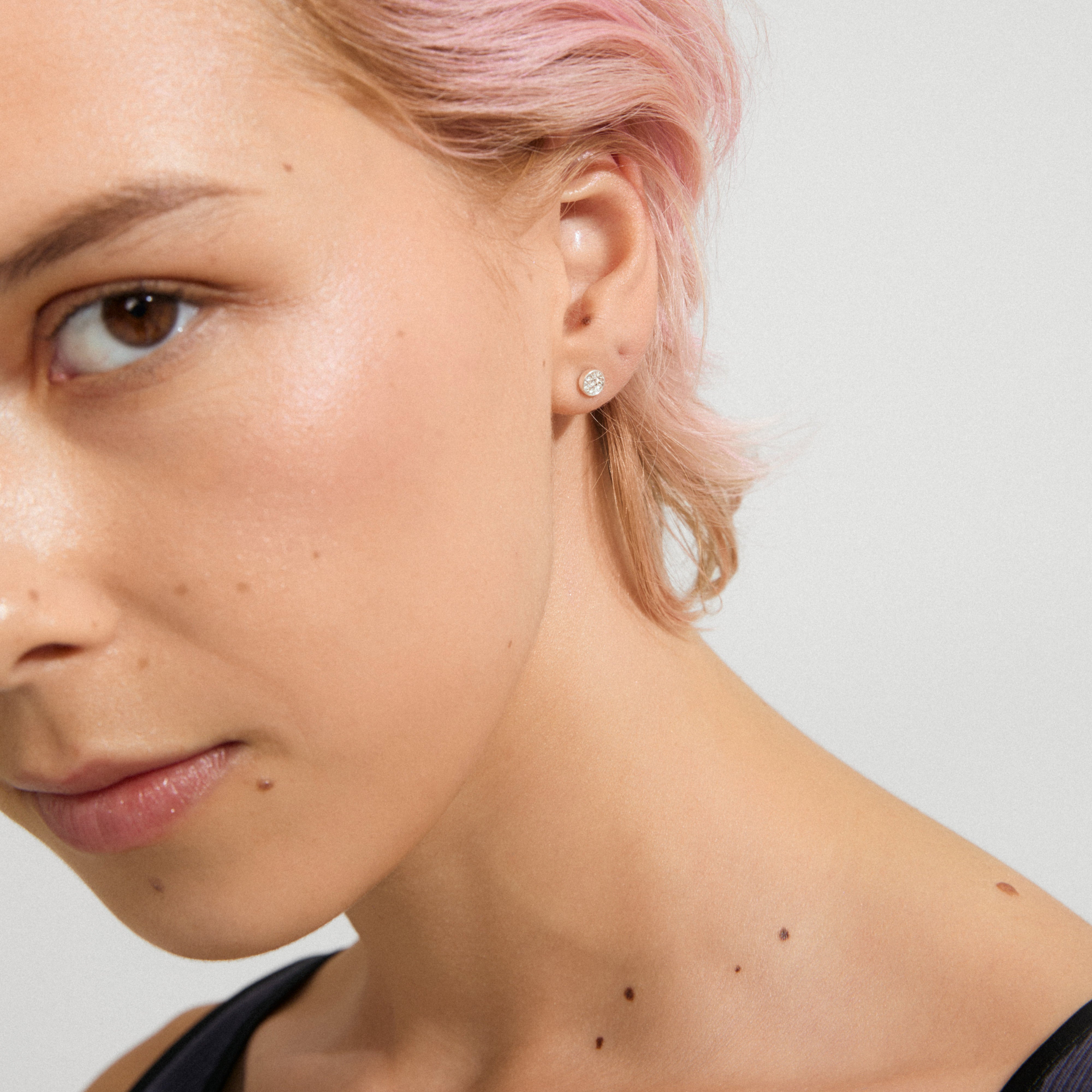 Person wearing EMMA crystal earrings, silver-plated, showcasing a minimalist design with clear sparkling crystals. Pastel pink hair and beauty marks accentuate the earring's elegance.
