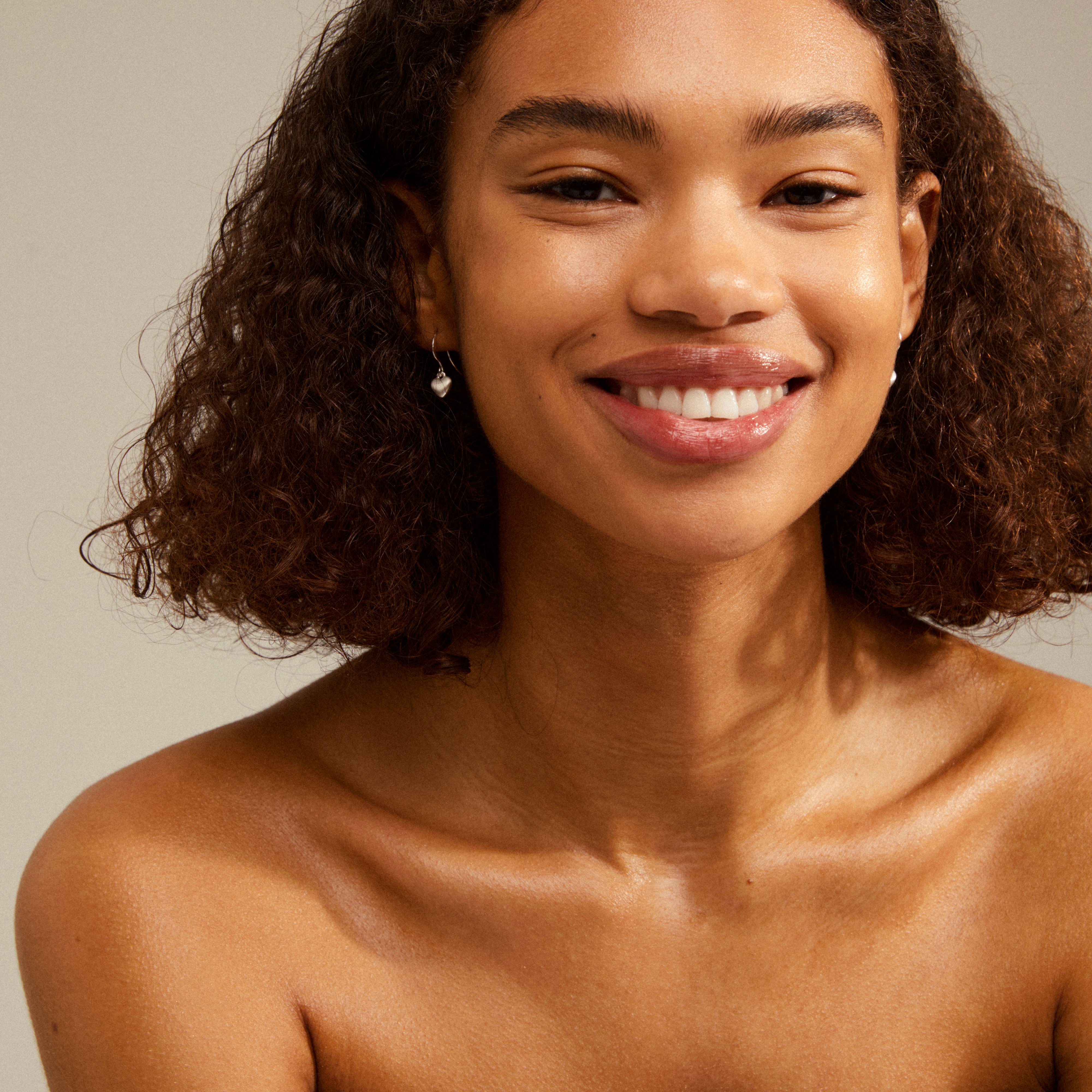SOPHIA heart pendant earrings, silver-plated, elegantly dangle from a smiling woman's ear, showcasing their velvet-matt finish.