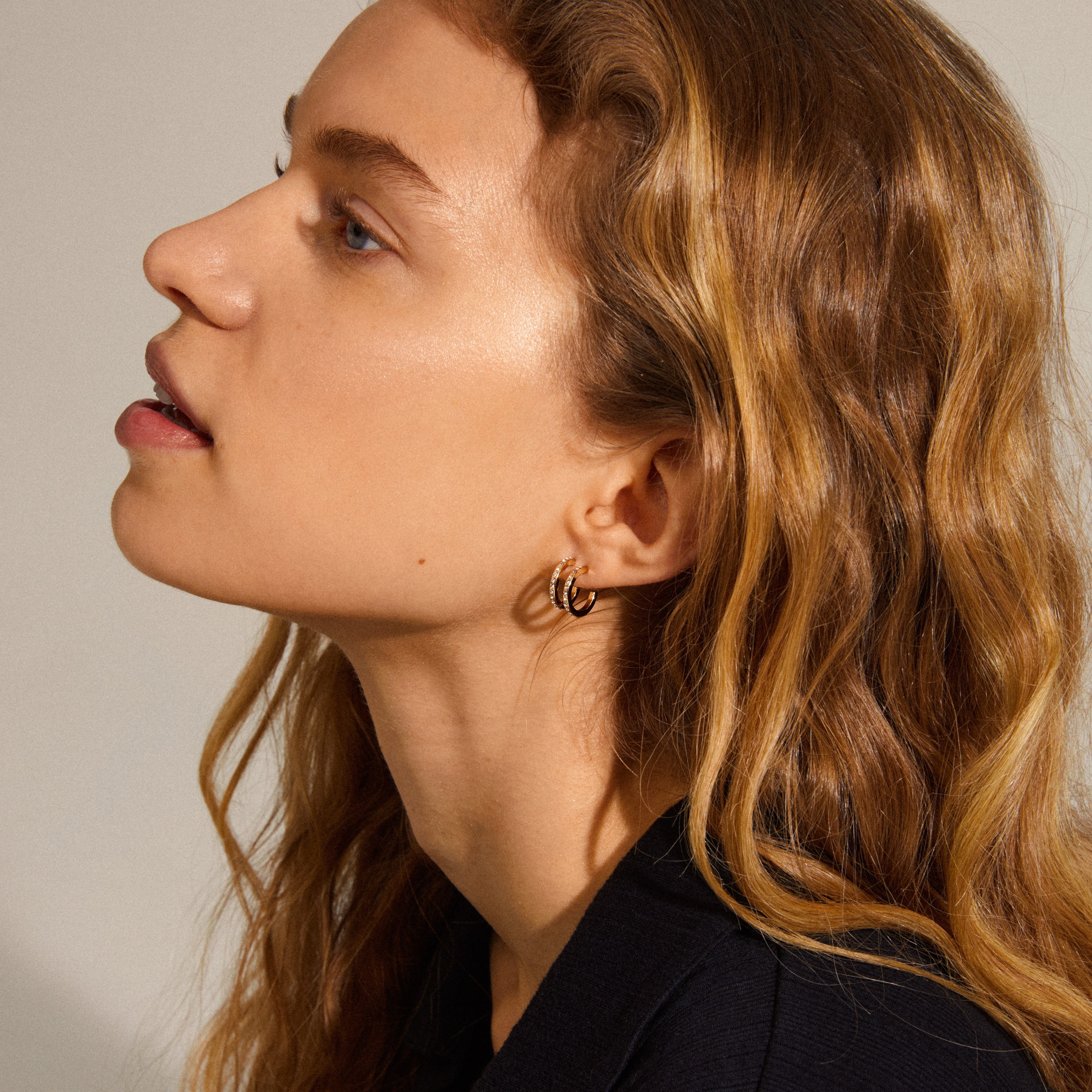 ROBERTA small crystal semi-hoops gold-plated, worn by a woman with long blonde hair, showcasing the elegant, sparkling crystals in a close-up of the ear.