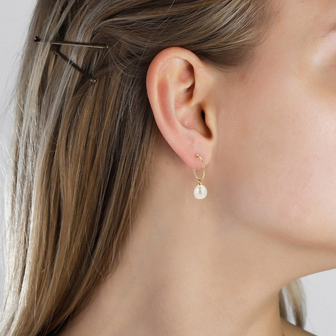 Close-up of a woman's ear wearing EILA gold-plated hoop earrings with pearl drops, showcasing a blend of classic and contemporary design elements.