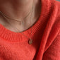 CLARA crystal cross necklace gold-plated on person, featuring a sparkling crystal-adorned cross pendant. The necklace is worn over a sweater.