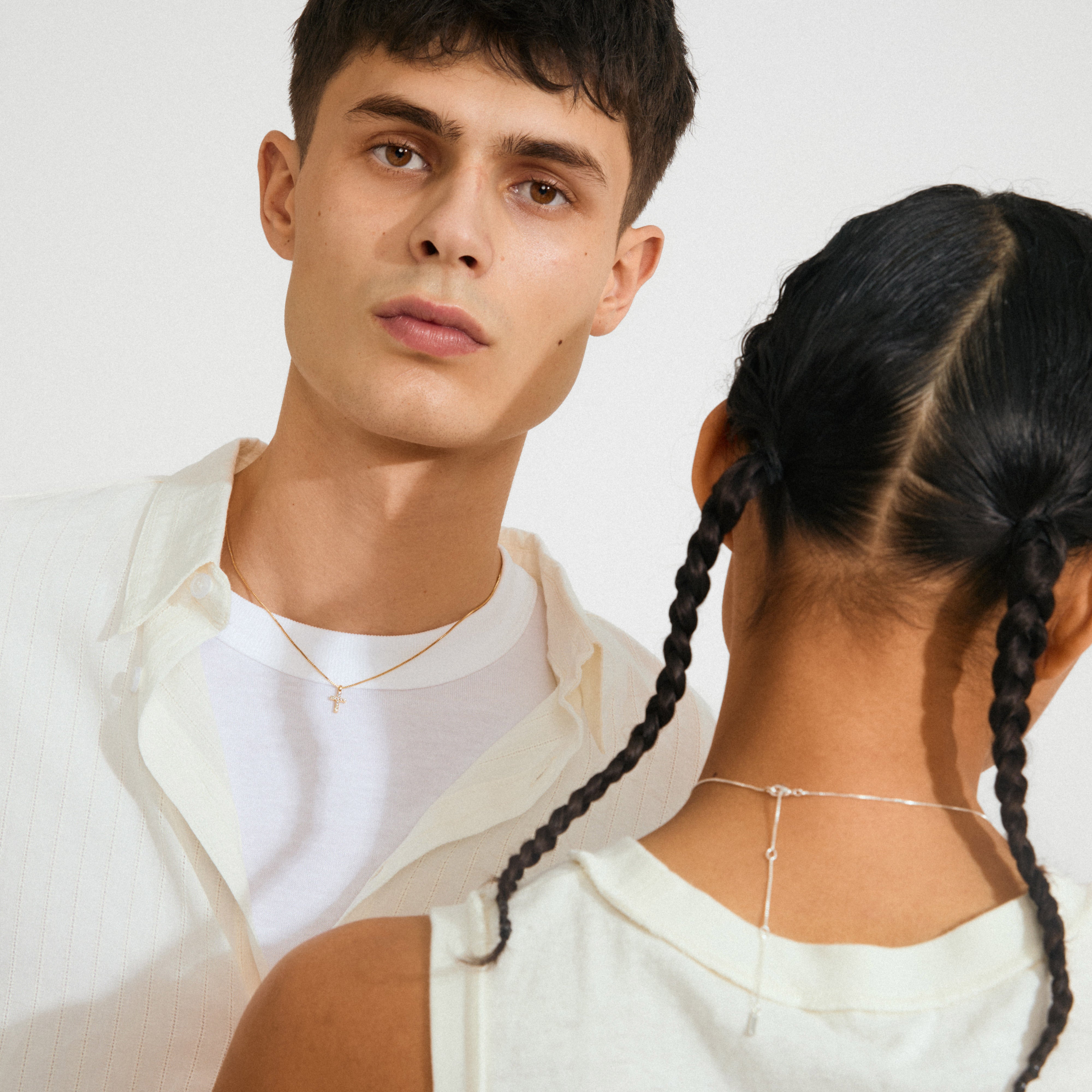 Two young adults showcase the CLARA crystal cross necklace gold-plated, highlighting its modern design with sparkling crystals on a delicate gold chain.