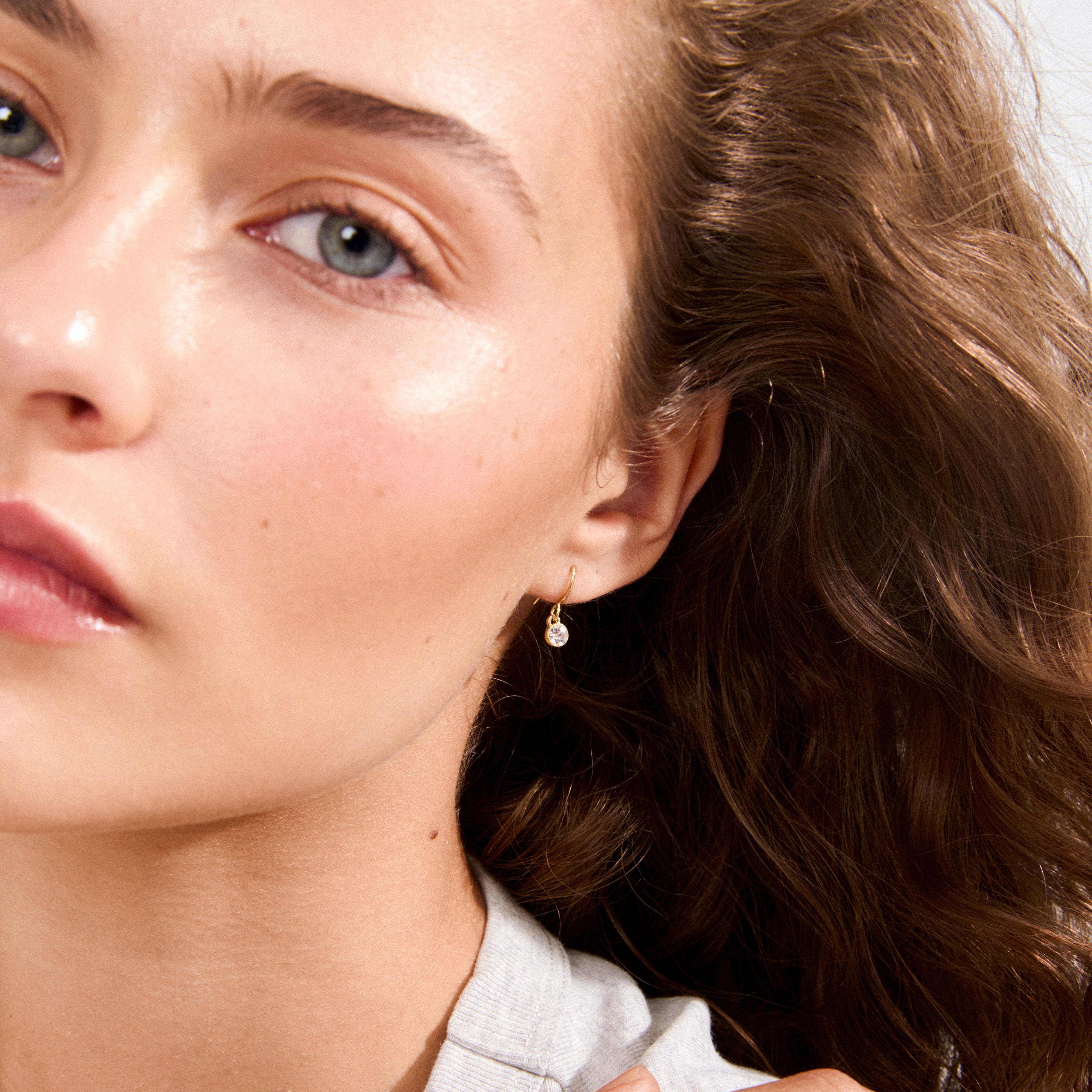 LUCIA crystal earrings gold-plated shimmer like morning dew on a young woman's ear, offering a subtle, enchanting touch perfect for casual elegance.