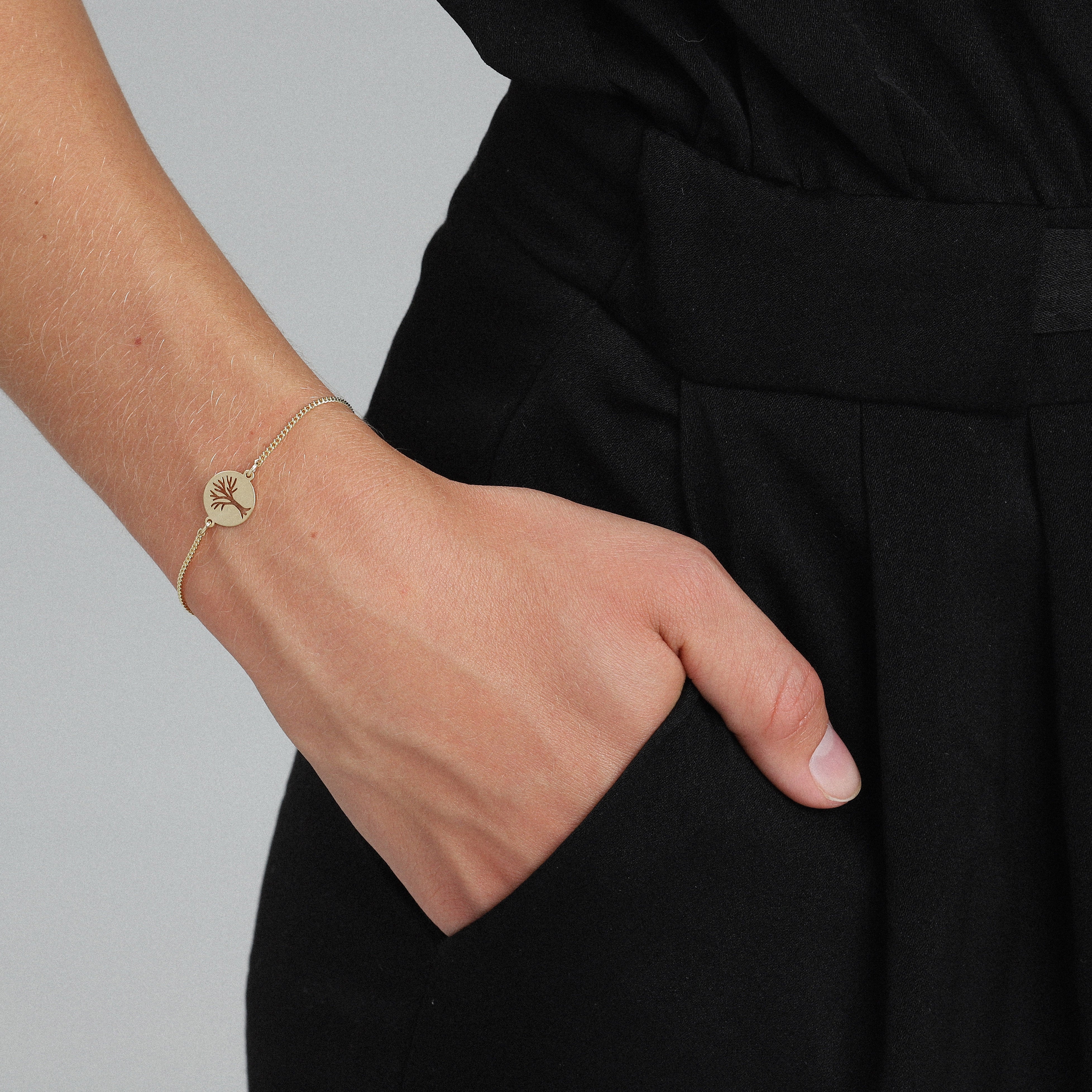 Person wearing ELIN coin bracelet gold-plated, featuring a slender chain and a circle with an etched tree motif, embodying chic Scandinavian style.