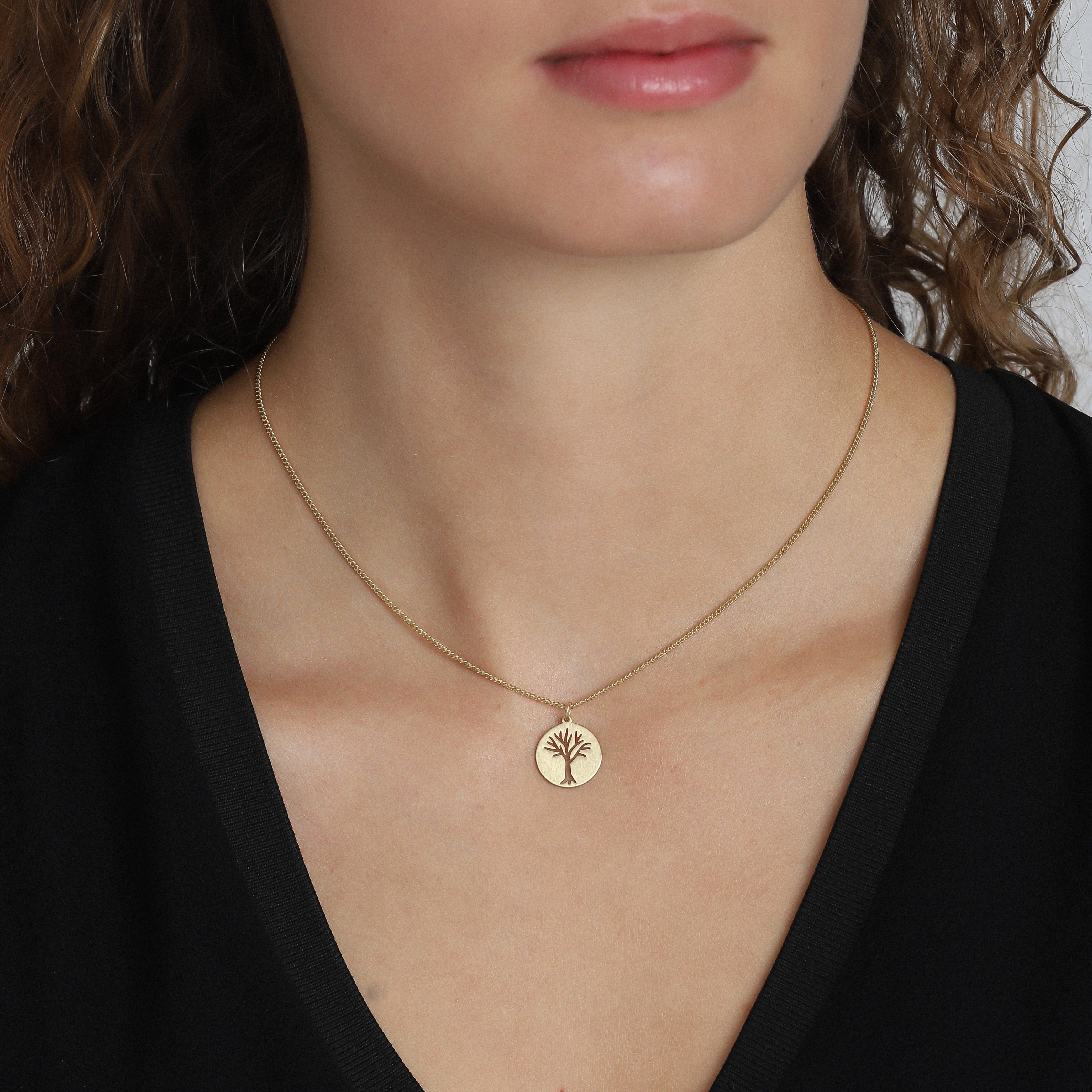 ELIN coin pendant necklace gold-plated featuring a tree silhouette on a matte circle, worn by a woman. Stylish and modern Scandinavian design.
