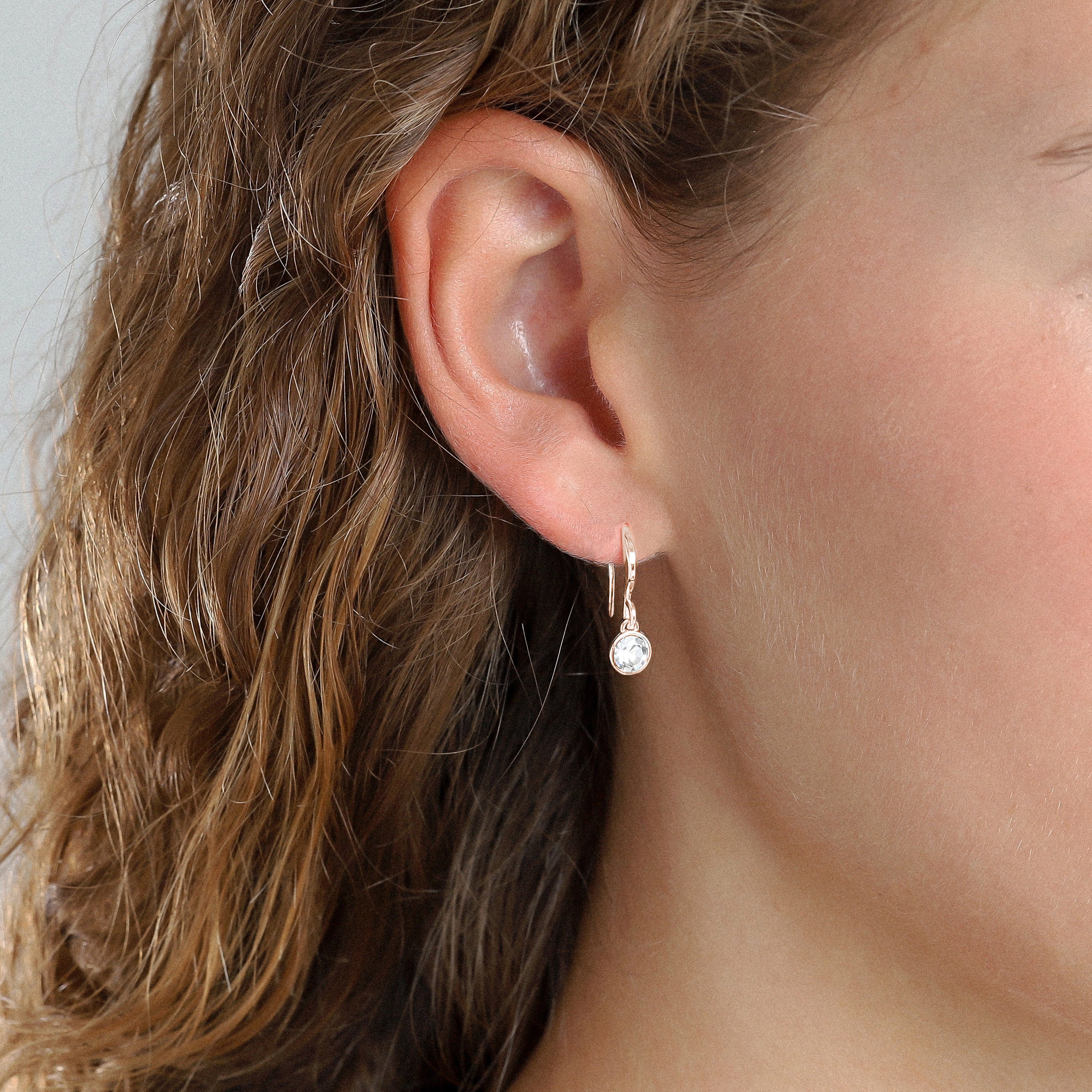 Close-up of a woman's ear wearing LUCIA rose gold-plated crystal earrings, showcasing their sparkling design and subtle elegance.