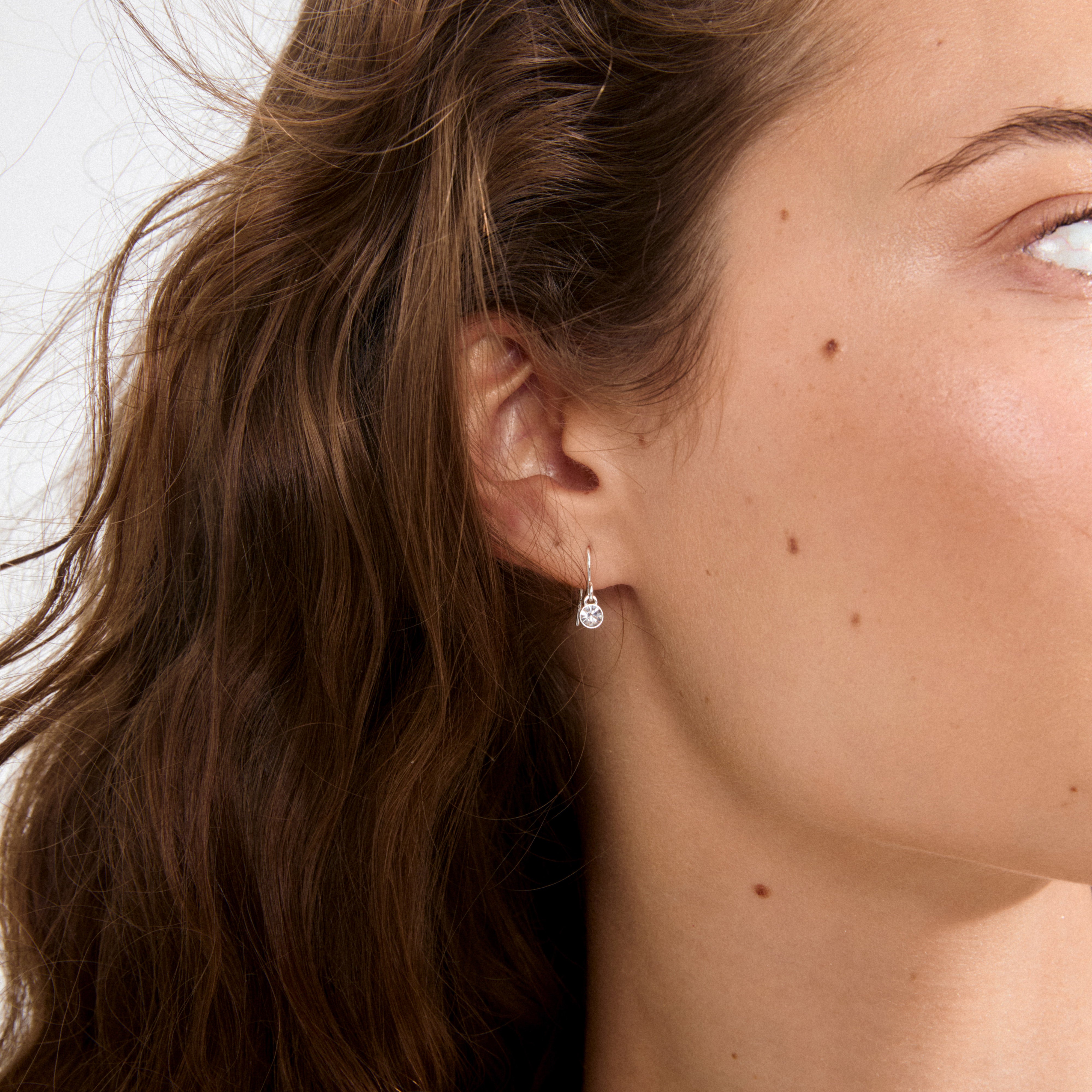 Young woman wearing LUCIA crystal earstuds silver-plated, showcasing delicate silver drop earrings with a faceted gemstone, embodying subtle elegance and Scandinavian craftsmanship.