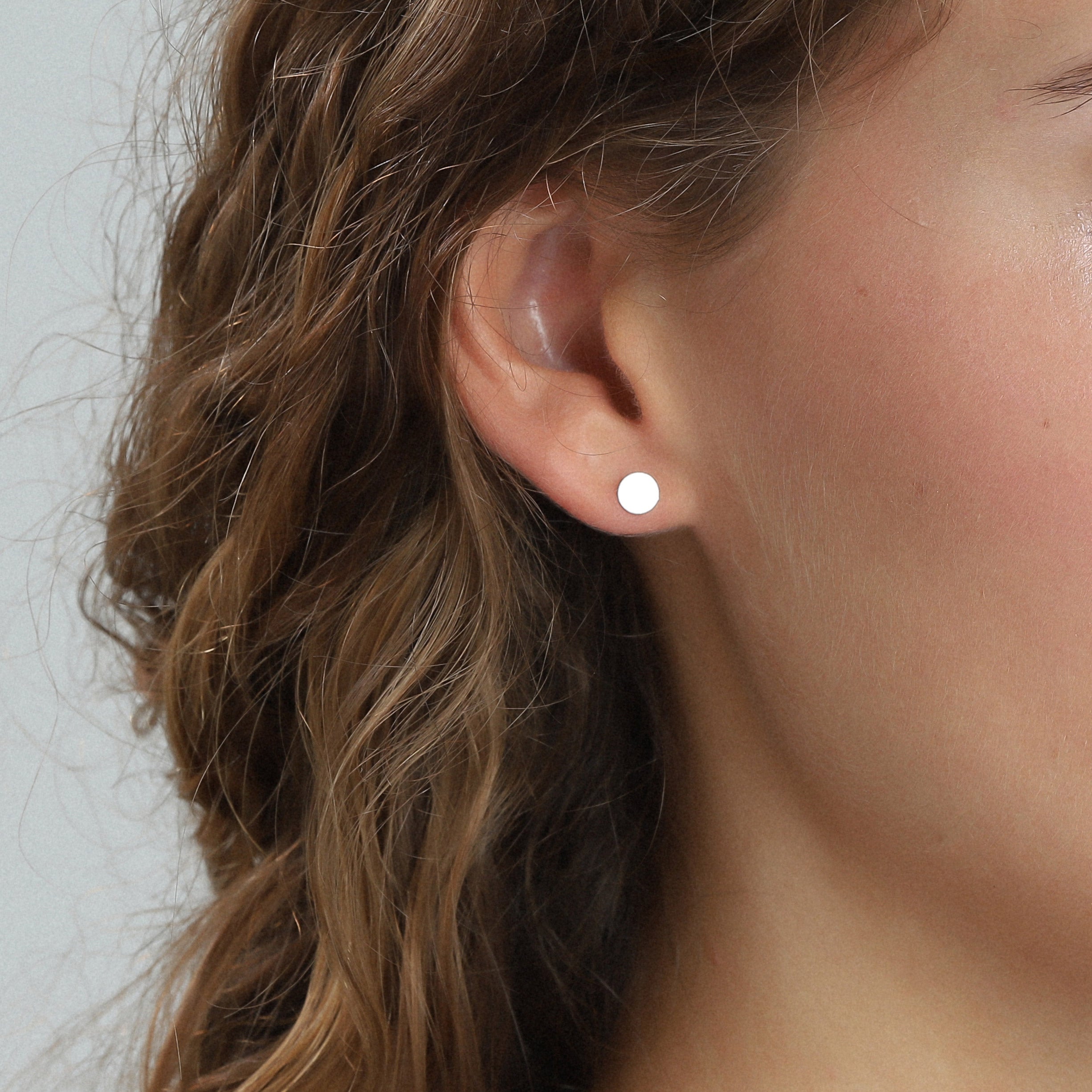 Close-up of a woman's ear wearing the NORMA 3-in-1 silver-plated earrings set, featuring minimalist studs in three sizes for versatile styling.
