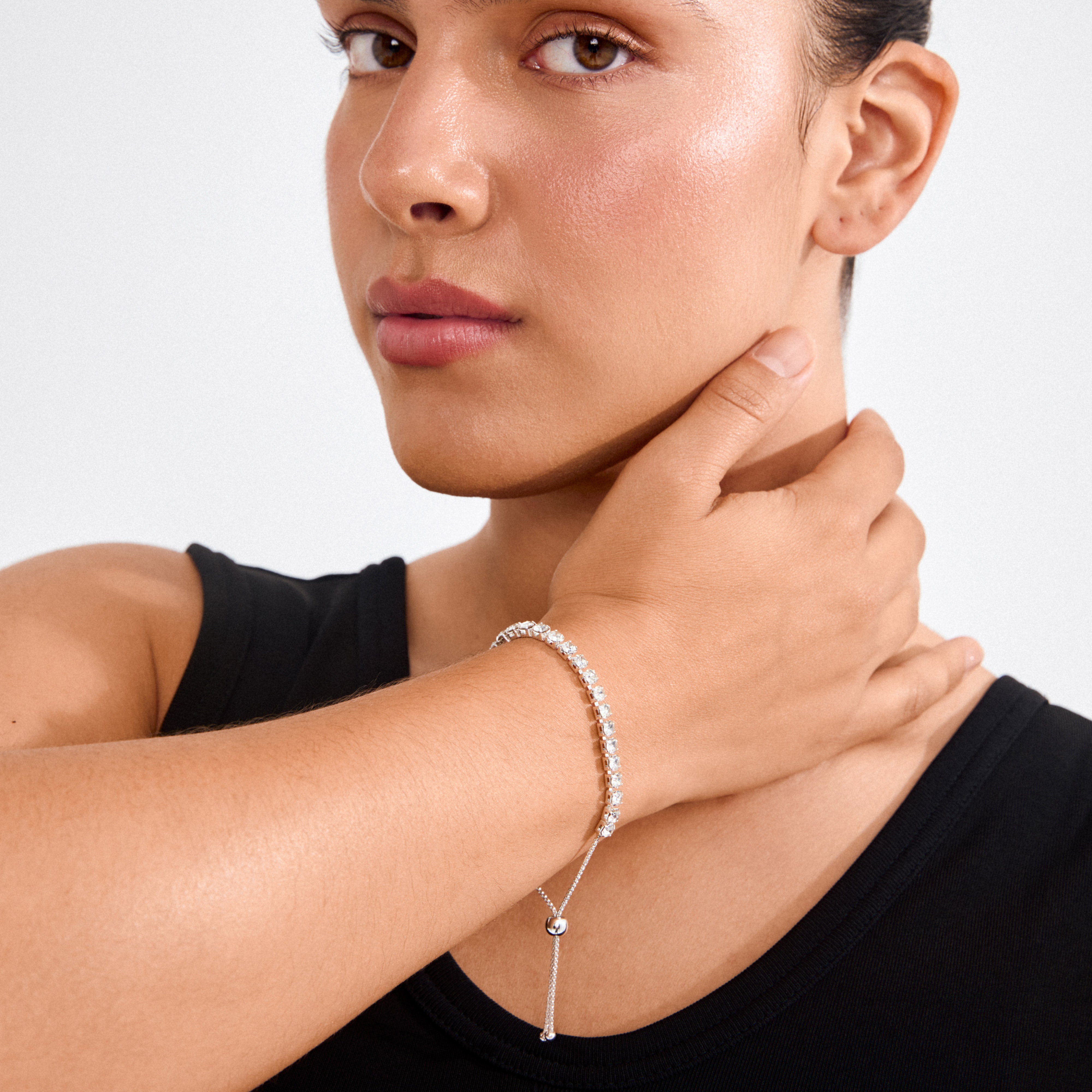 Woman wearing LUCIA crystal bracelet, silver-plated with clear Preciosa crystals, cupping neck. Bracelet sparkles elegantly, showcasing its adjustable, eco-friendly design.