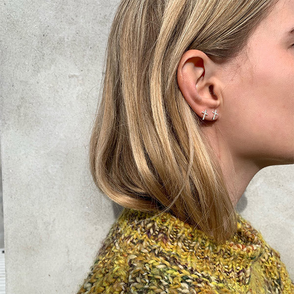 Woman wearing CLARA crystal cross earrings, silver-plated, with sparkling crystals, highlighting elegance and style. Perfect for trendsetters seeking unique, feminine accessories.