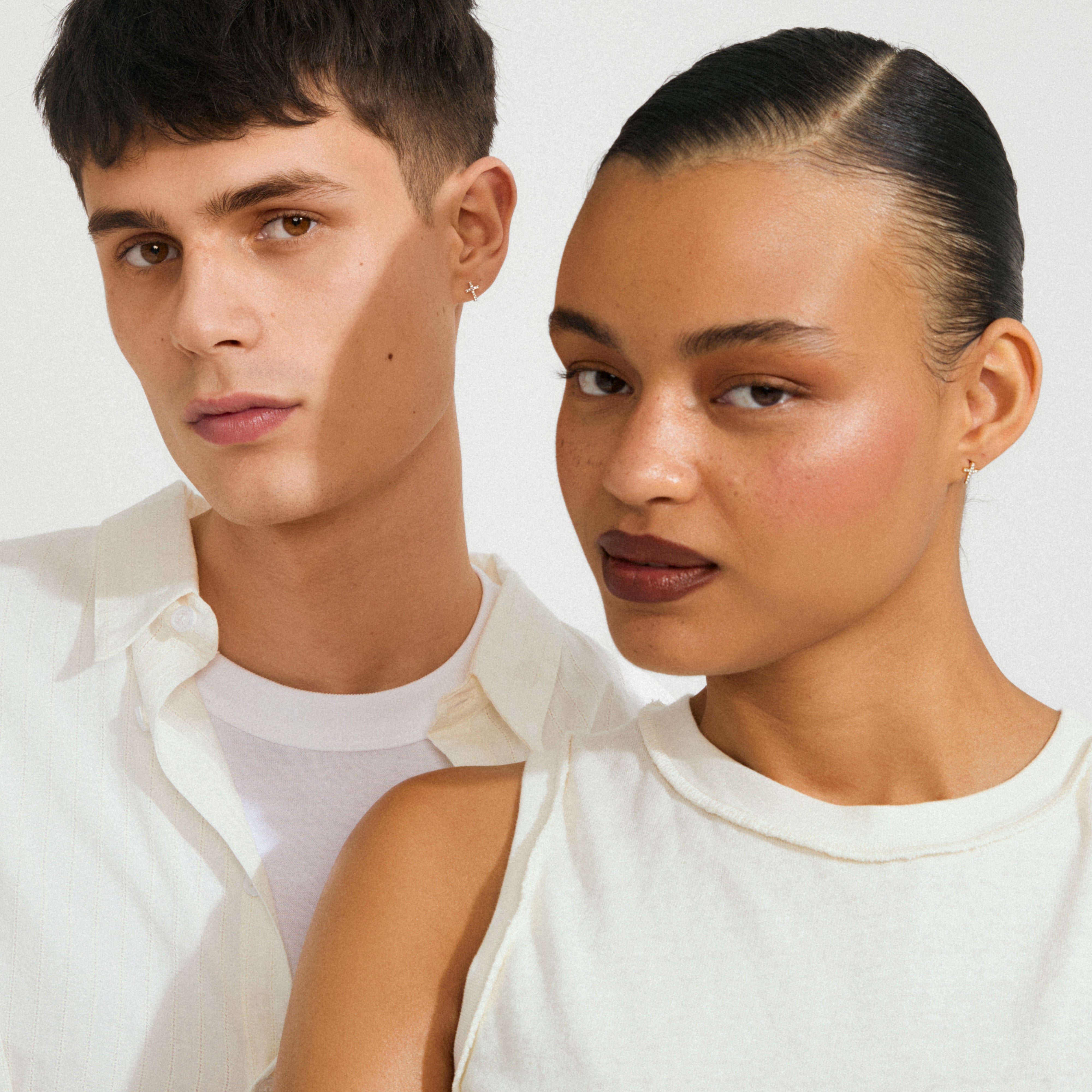 Two models wear CLARA crystal cross earrings, showcasing the silver-plated studs' sparkling crystals on clean, natural makeup, highlighting their elegant simplicity and modern design.