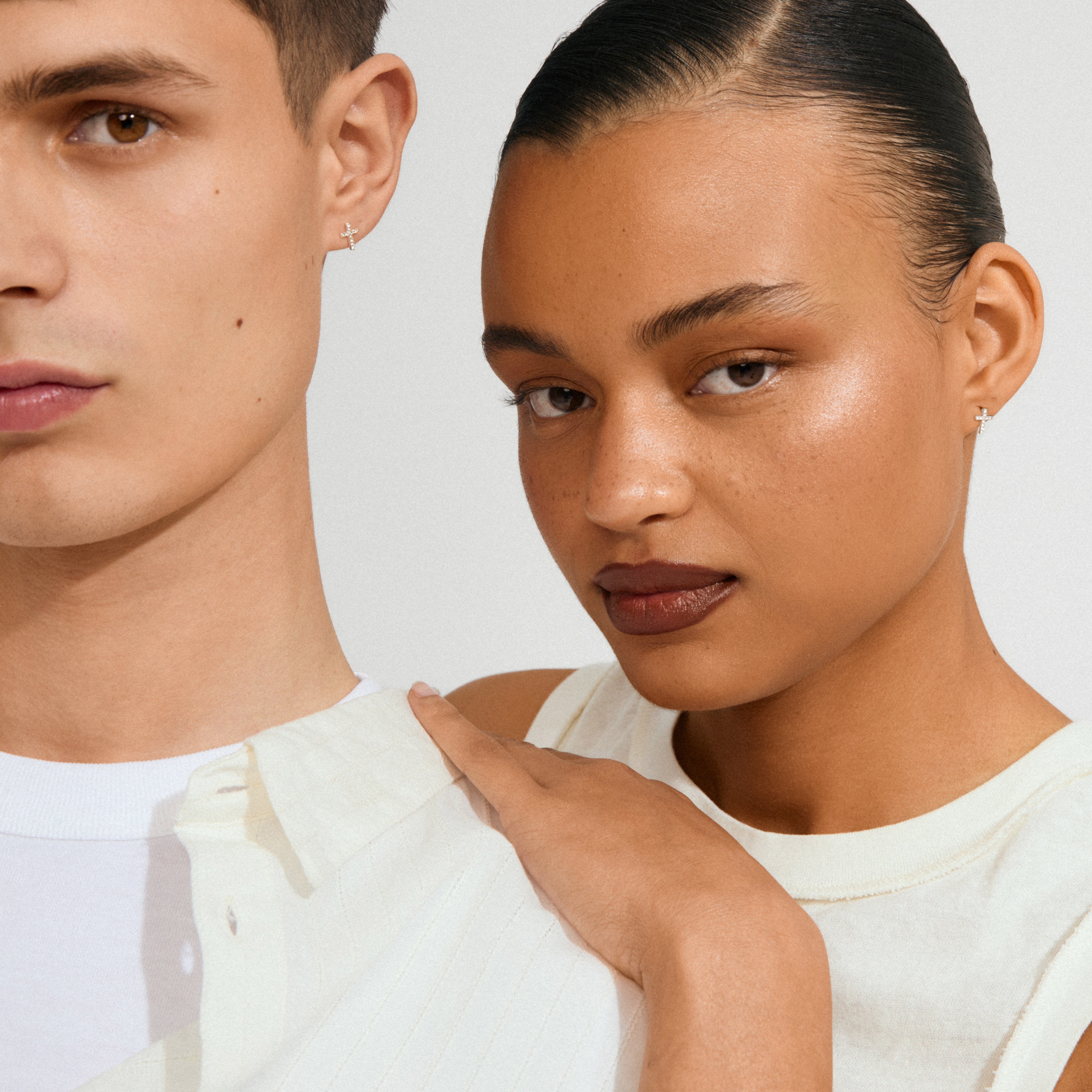 Two young adults wearing CLARA crystal cross earrings silver-plated, showcasing sparkling crystals that highlight the earrings' unique, feminine design against a neutral backdrop.